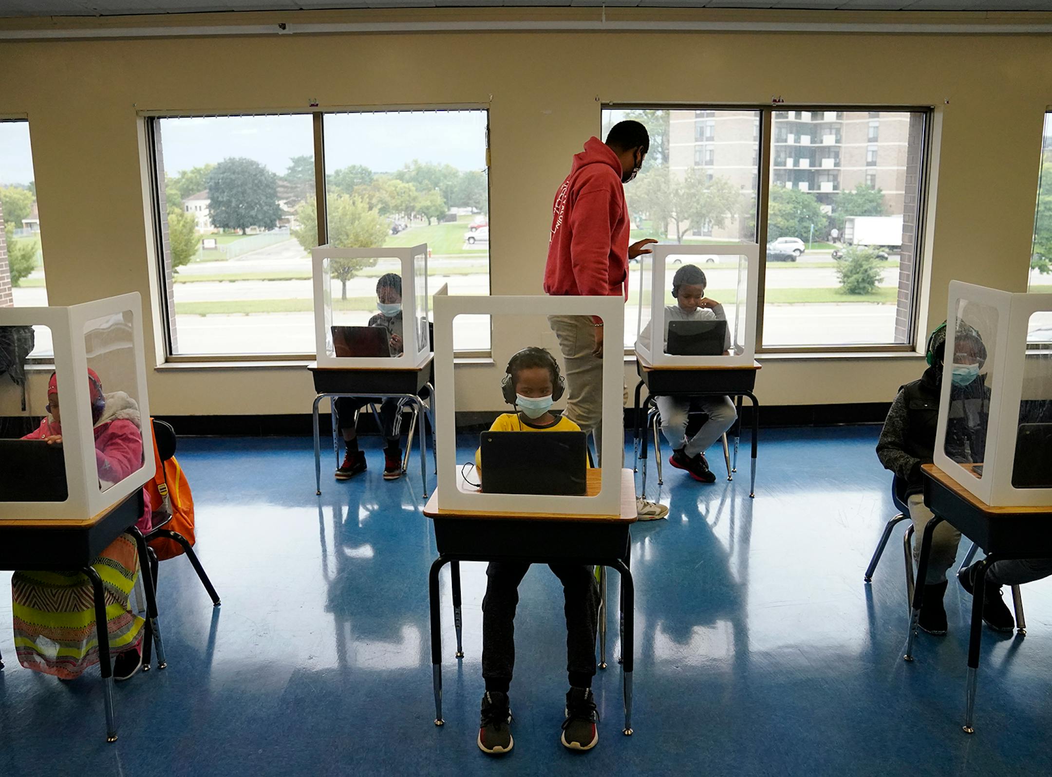 It was back to school for some students at Harvest Best Academy Tuesday in Minneapolis, but with masks, plastic barriers and other new precautions in the era of COVID-19. Here, para professional Jaevon Walton, middle, reminded a student to wear his face mask in a learning pod of 2nd through 7th graders.