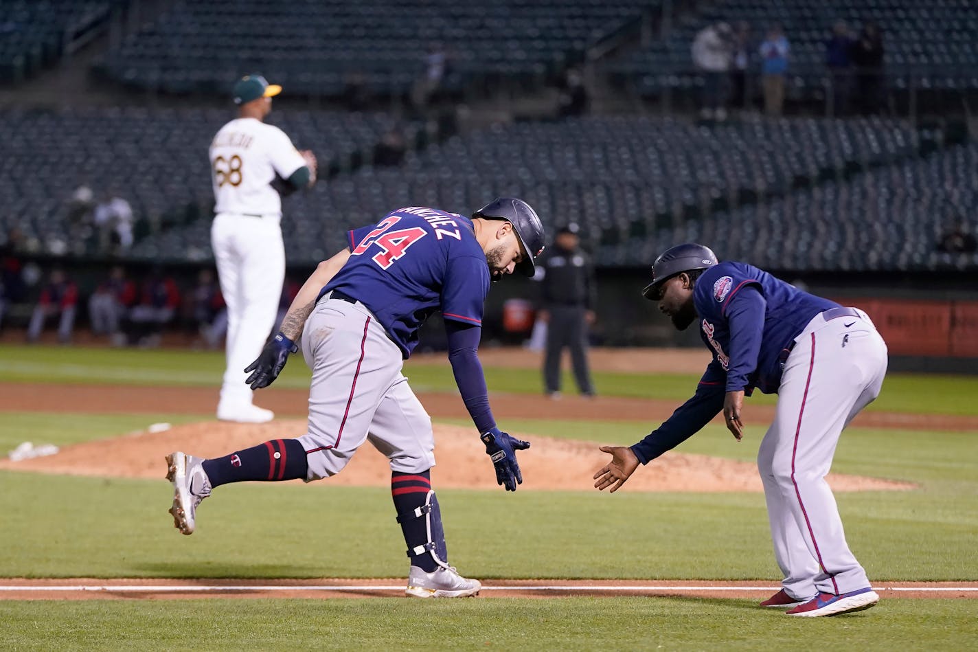 Minnesota Twins' Gary Sanchez, bottom left, is congratulated by third base coach Tommy Watkins after hitting a home run off of Oakland Athletics pitcher Domingo Acevedo, rear, during the sixth inning of a baseball game in Oakland, Calif., Monday, May 16, 2022. (AP Photo/Jeff Chiu)