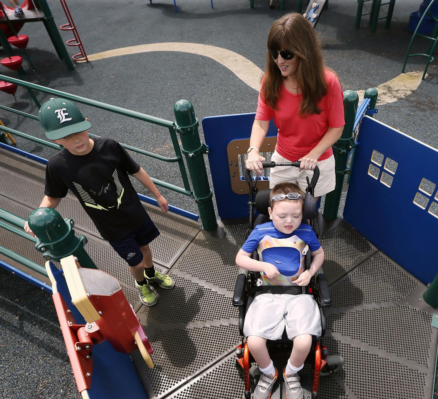 Suzanne Sullivan pushed her son Dermot across the walk way in his wheel chair .Dermot has a mitochondrial disorder but is able to play with his two brothers on an inclusive playground at Alice Smith Elementary Monday June 23, 2014 in Hopkins, MN. The two brothers are Owen 10 left , and Ryan age 6 on right who is not in the photo. ] Jerry Holt Jerry.holt@startribune.com