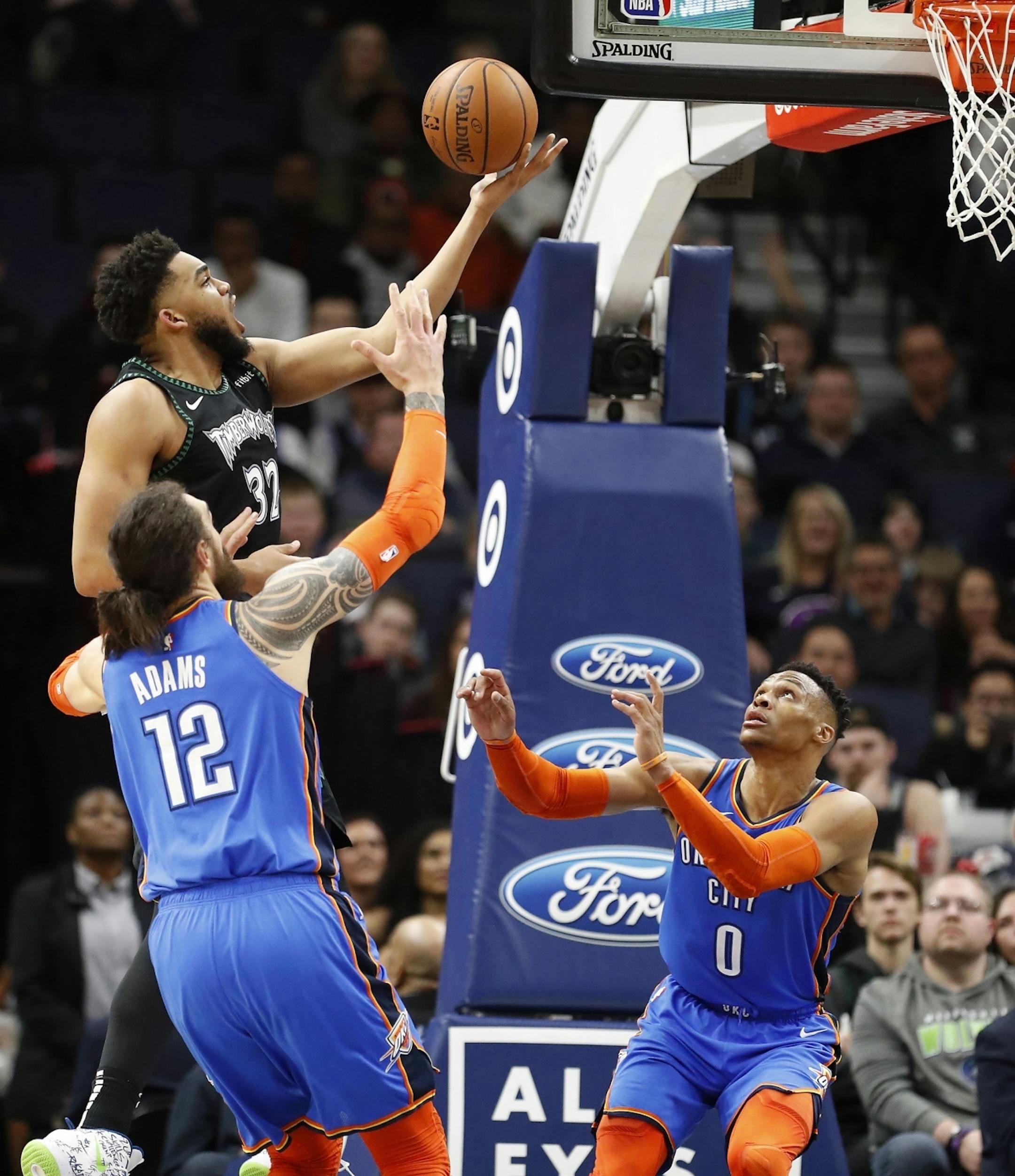Minnesota Timberwolves center Karl-Anthony Towns (32) shoots as Oklahoma City Thunder center Steven Adams (12) and Oklahoma City Thunder guard Russell Westbrook (0) defend during the second half.