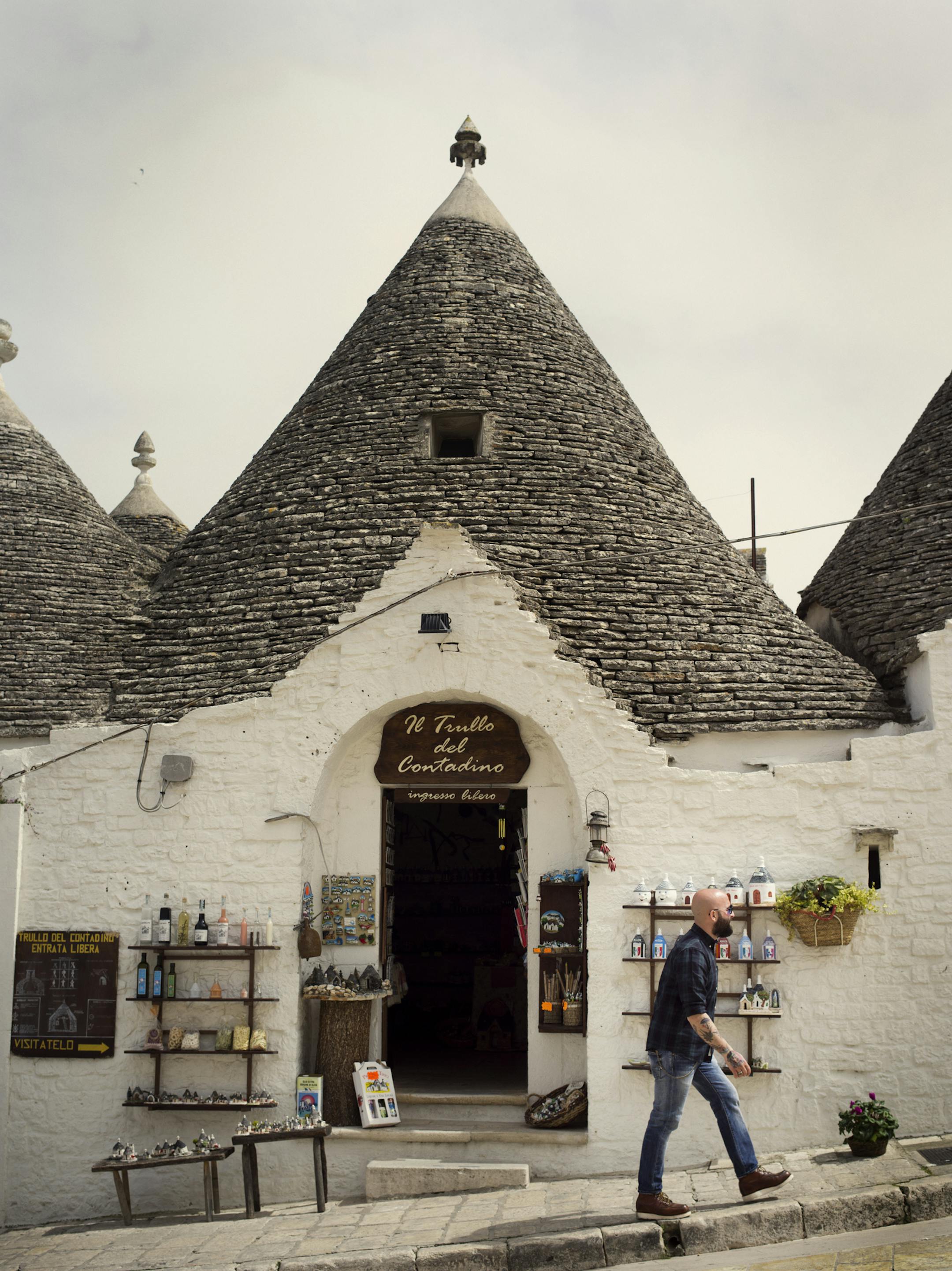 A man walks in front of a tourist shop in Alberobello, in Italy's Puglia region. The city is known for its trulli, or little white houses with conical roofs. The roofs are built by stacking rings of stones. MUST CREDIT: Photo by Lorenzo Pesce for The Washington Post. ORG XMIT: 104.0.1031326033