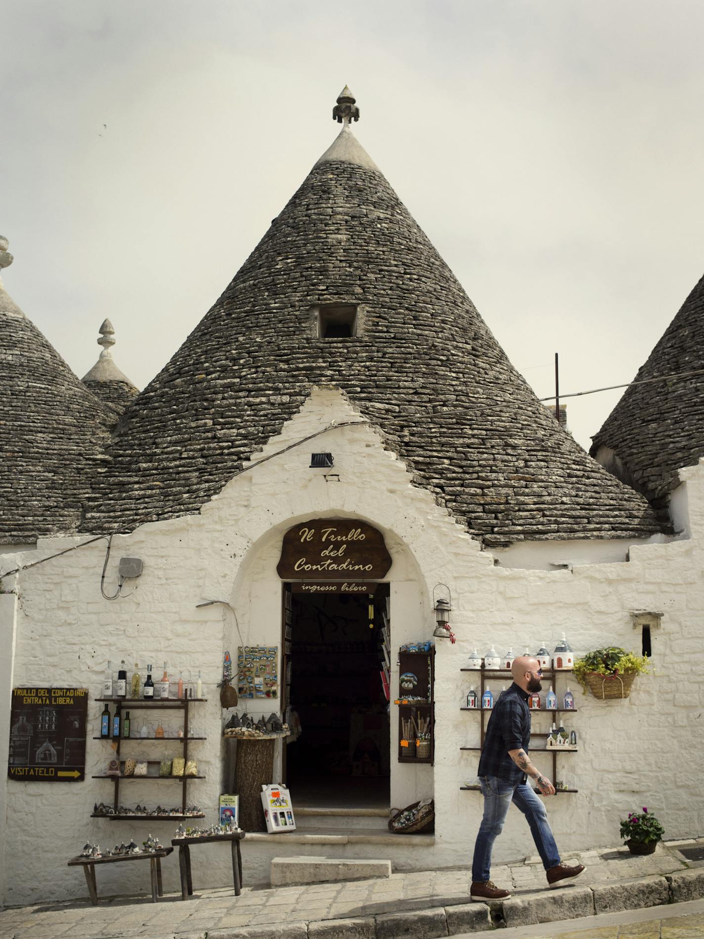 A man walks in front of a tourist shop in Alberobello, in Italy's Puglia region. The city is known for its trulli, or little white houses with conical roofs. The roofs are built by stacking rings of stones. MUST CREDIT: Photo by Lorenzo Pesce for The Washington Post. ORG XMIT: 104.0.1031326033