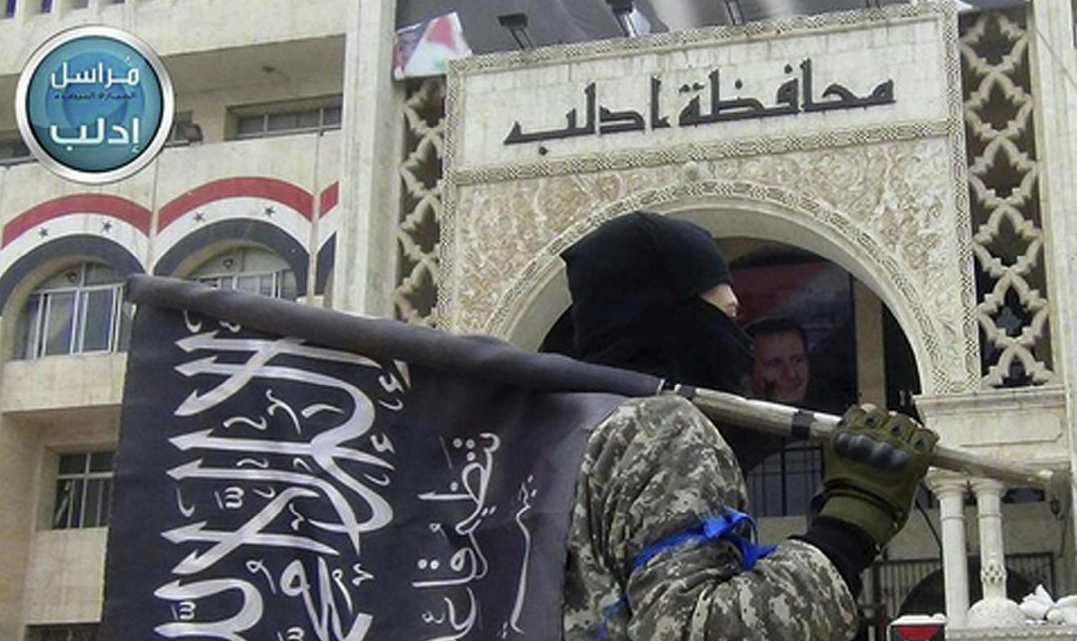 FILE - In this file photo posted on the Twitter page of Syria's al-Qaida-linked Nusra Front March 28, 2015, which is consistent with AP reporting, a fighter from Syria's al-Qaida-linked Nusra Front holds his group flag in front of an Idlib governorate building in Idlib province, north Syria. London-based Amnesty International said in a report released Tuesday, July 5, 2016, that some opposition groups in Syria have adopted methods of abuse similar to those employed by the government, after docum