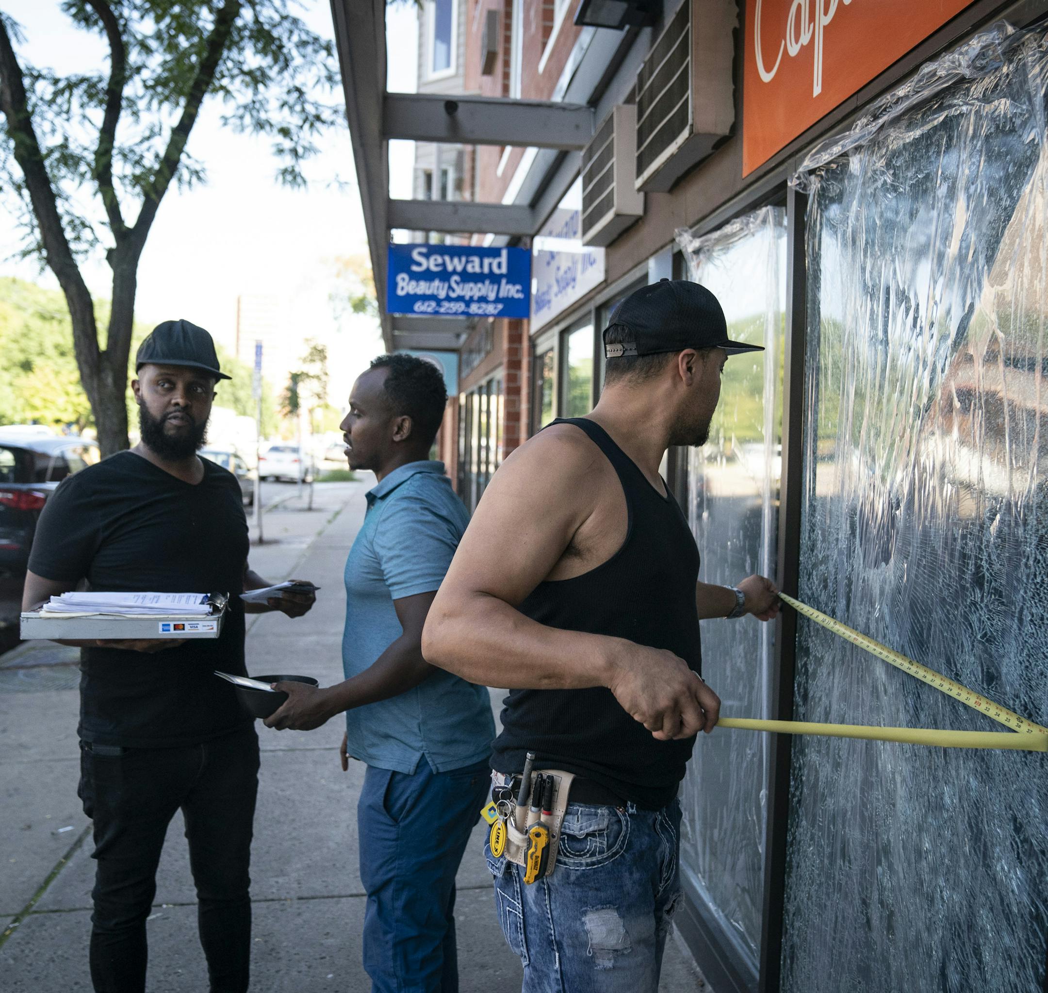 John Torgeson, right, who works in emergency glass services, measured the windows at the Capitol Cafe to give Burhan Elmi, co-owner of the cafe, left, and manager Abdi Awad, center, a quote for the repair. Two large windows at the Capitol Cafe and several other store windows were damaged along Franklin Avenue by a vandal recently in Minneapolis, Minn., on Thursday, September 19, 2019. ] RENEE JONES SCHNEIDER ¥ renee.jones@startribune.com