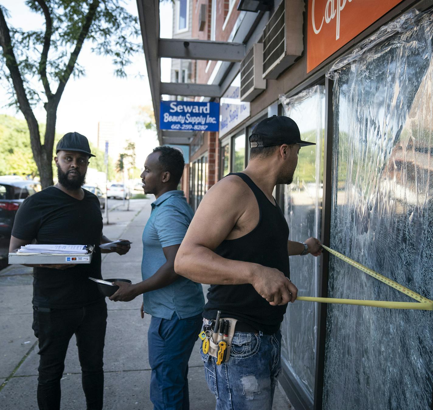 John Torgeson, right, who works in emergency glass services, measured the windows at the Capitol Cafe to give Burhan Elmi, co-owner of the cafe, left, and manager Abdi Awad, center, a quote for the repair. Two large windows at the Capitol Cafe and several other store windows were damaged along Franklin Avenue by a vandal recently in Minneapolis, Minn., on Thursday, September 19, 2019. ] RENEE JONES SCHNEIDER &#xa5; renee.jones@startribune.com