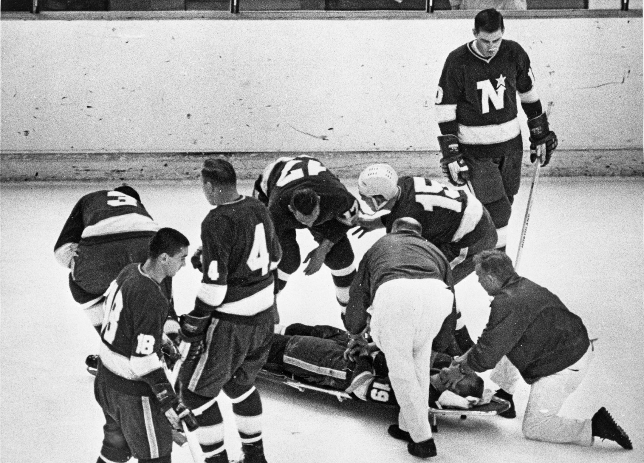 Photo ran: January 15, 1968, Minneapolis Tribune
Caption: Injured. Bill Masterton, North Star center, was taken unconscious from Saturday night's game with Oakland after sustaining head injuries early in the first period of the 2-2 game. Trainer Stan Waylett and assistant trainer Al Schuenman (kneeling) helped slide the stretcher toward the exit Masterton remained unconscious in critical condition Sunday. Other North Star players are Bob McCord (3), Bill Collins (18), Elmer Vasko (4), Dave Balon