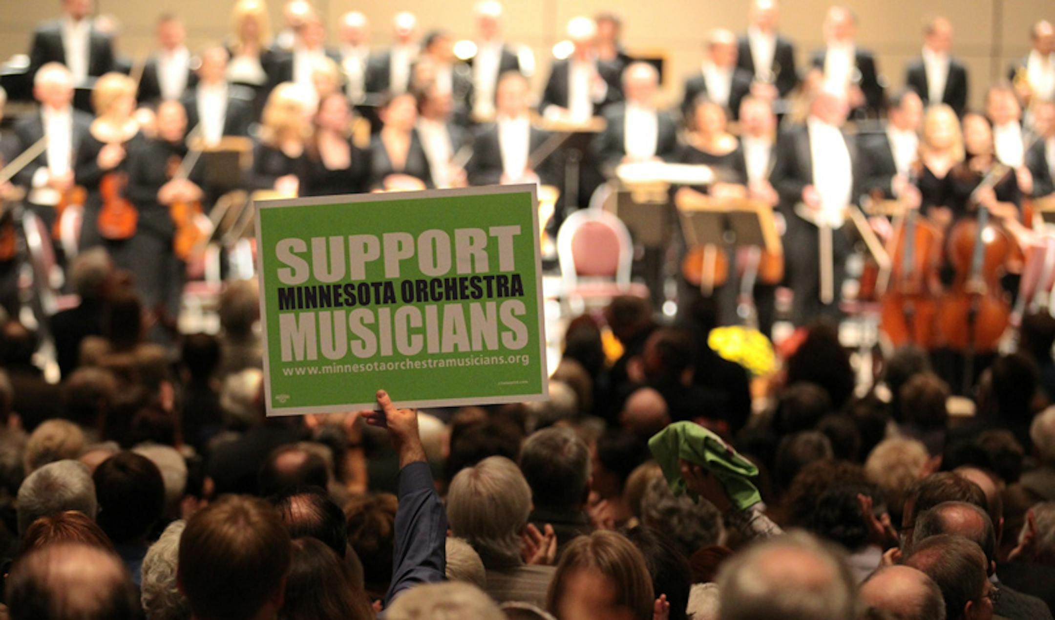 A packed audience gave a standing ovation, and held up a sign in support, to the musicians of the Minnesota orchestra at a concert held at the Minneapolis Convention Center on Oct. 18, 2012.