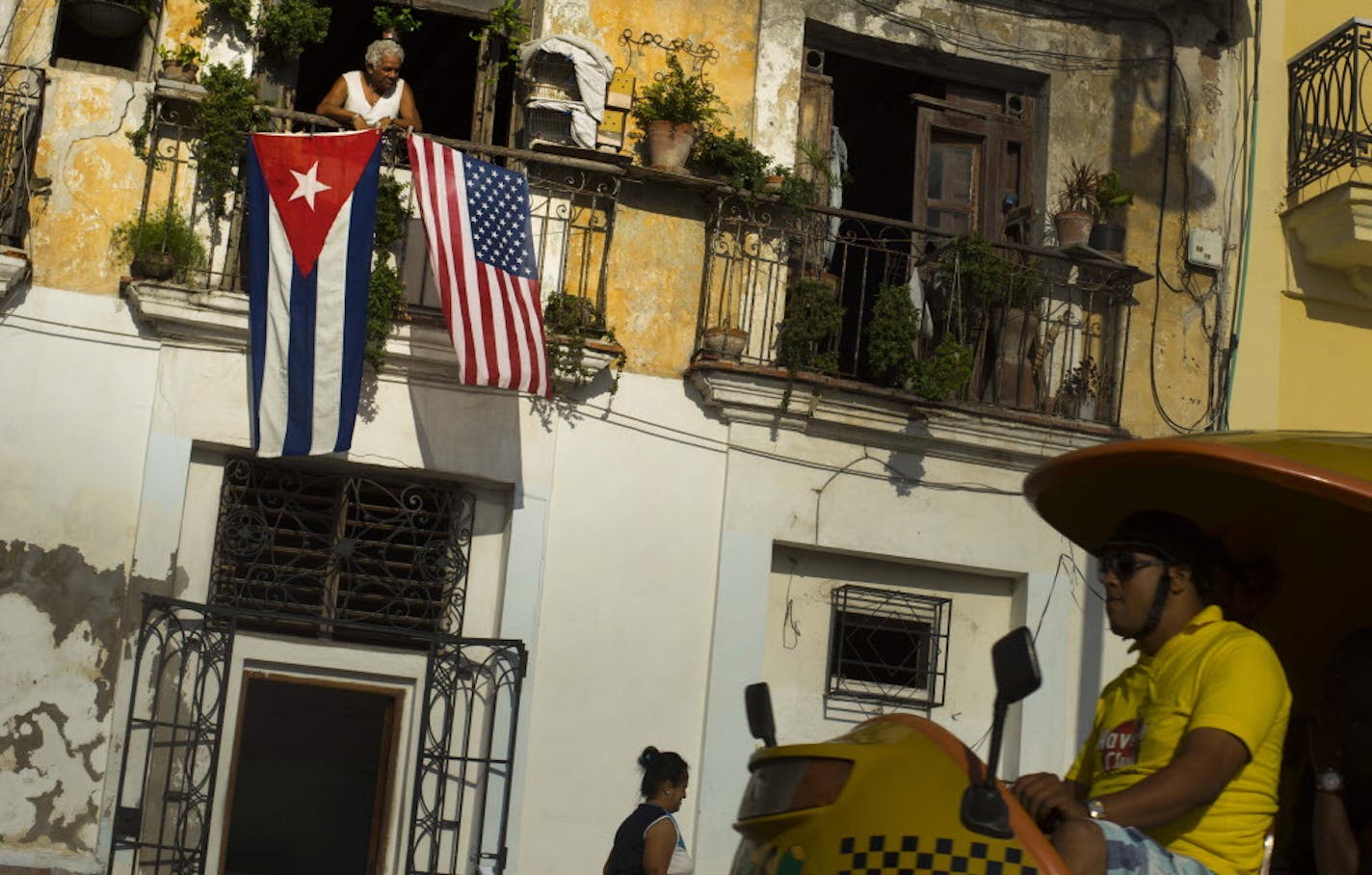 FILE - In this July 20, 2015, file photo, Javier Yanez looks out from his balcony where he hung a U.S., and a Cuban national flag, to celebrate the restored full diplomatic relations between Cuba and the Unites States, in Old Havana. The U.S. Commerce Department said Tuesday, Jan. 26 2016, that it would now allow U.S. exports to Cuban government agencies in cases where it believed the Cuban people stood to benefit. (AP Photo/Ramon Espinosa, File)