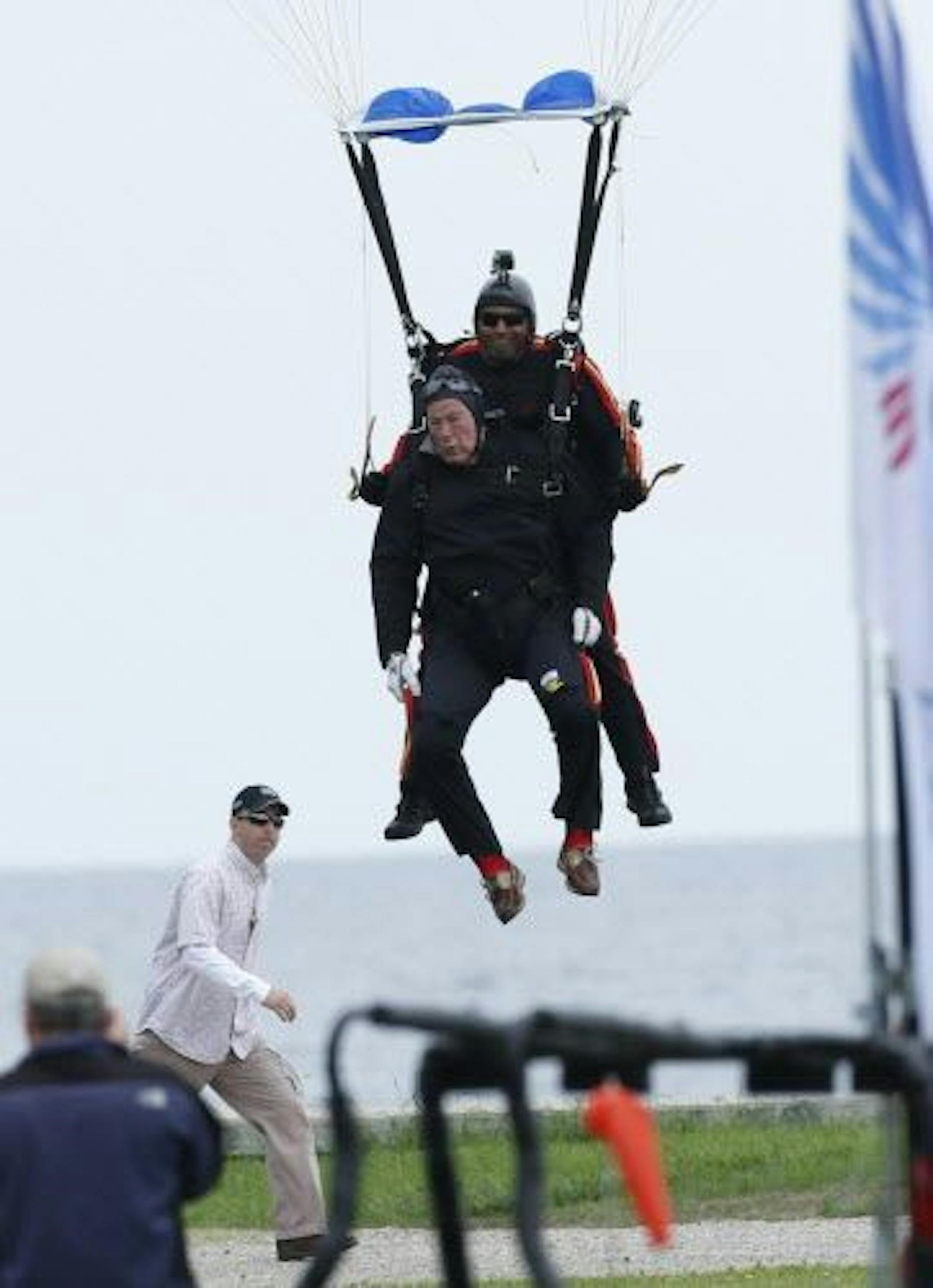 Former President George H.W. Bush, strapped to Sgt. 1st Class Mike Elliott, a retired member of the Army's Golden Knights parachute team, prepare to land on the lawn at St. Anne's Episcopal Church while celebrating Bush's 90th birthday in Kennebunkport, Maine, Thursday, June 12, 2014.