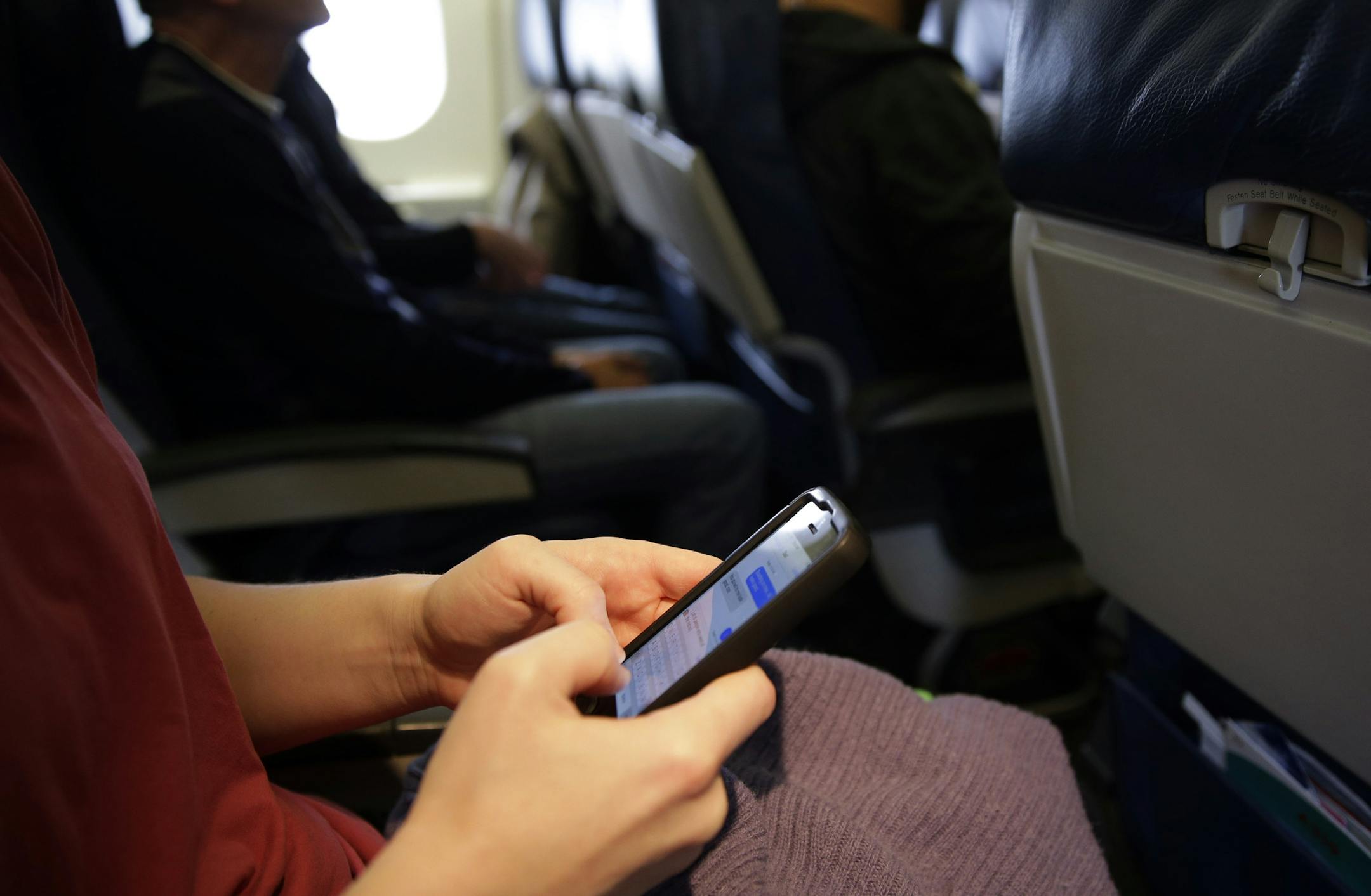 FILE - In this Oct. 31, 2013, file photo, a passenger checks her cell phone before a flight in Boston. Federal regulators said Thursday, Nov. 21, 2013, that rules against making cellphone calls during airline flights are "outdated," and it's time to change them. The Federal Aviation Administration recently lifted restrictions on the use of most personal electronic devices during takeoffs and landings, but not cellphone calls, which fall under the FCC. (AP Photo/Matt Slocum, File)