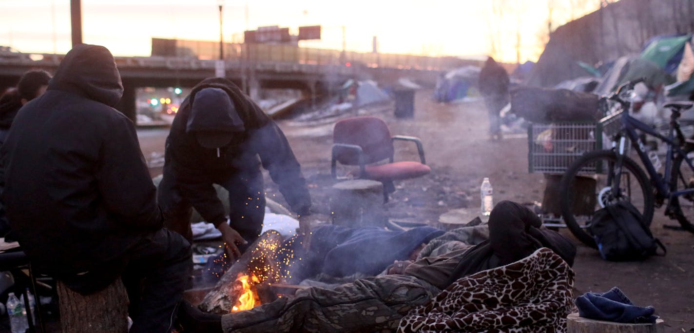 The final residents of the large homeless camp in south Minneapolis departed on Friday. Here, in what may have been the last camp fire to burn at the encampment residents warm themselves along Franklin Avenue.