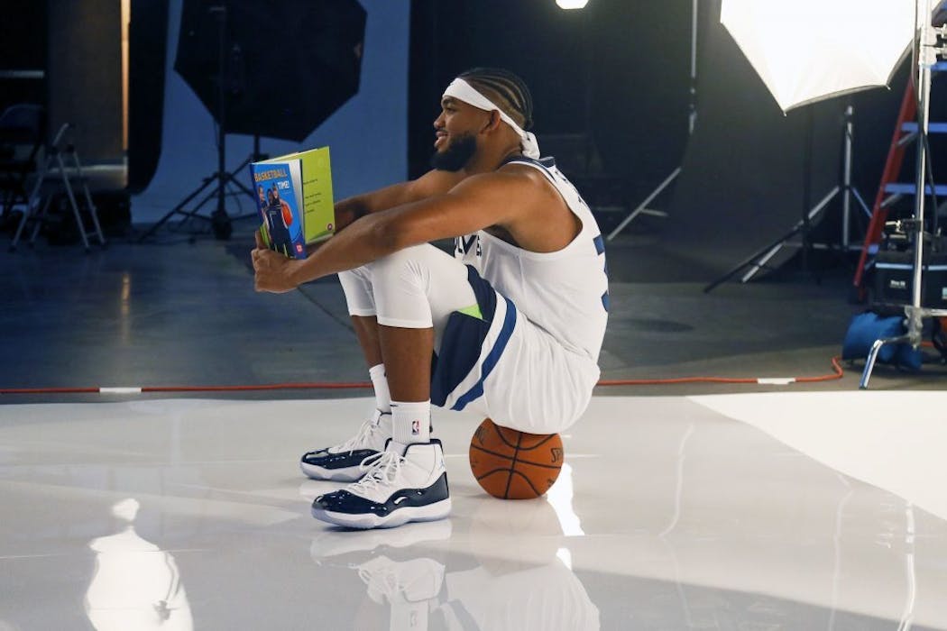 Karl-Anthony Towns sits on a ball while holding children's book.