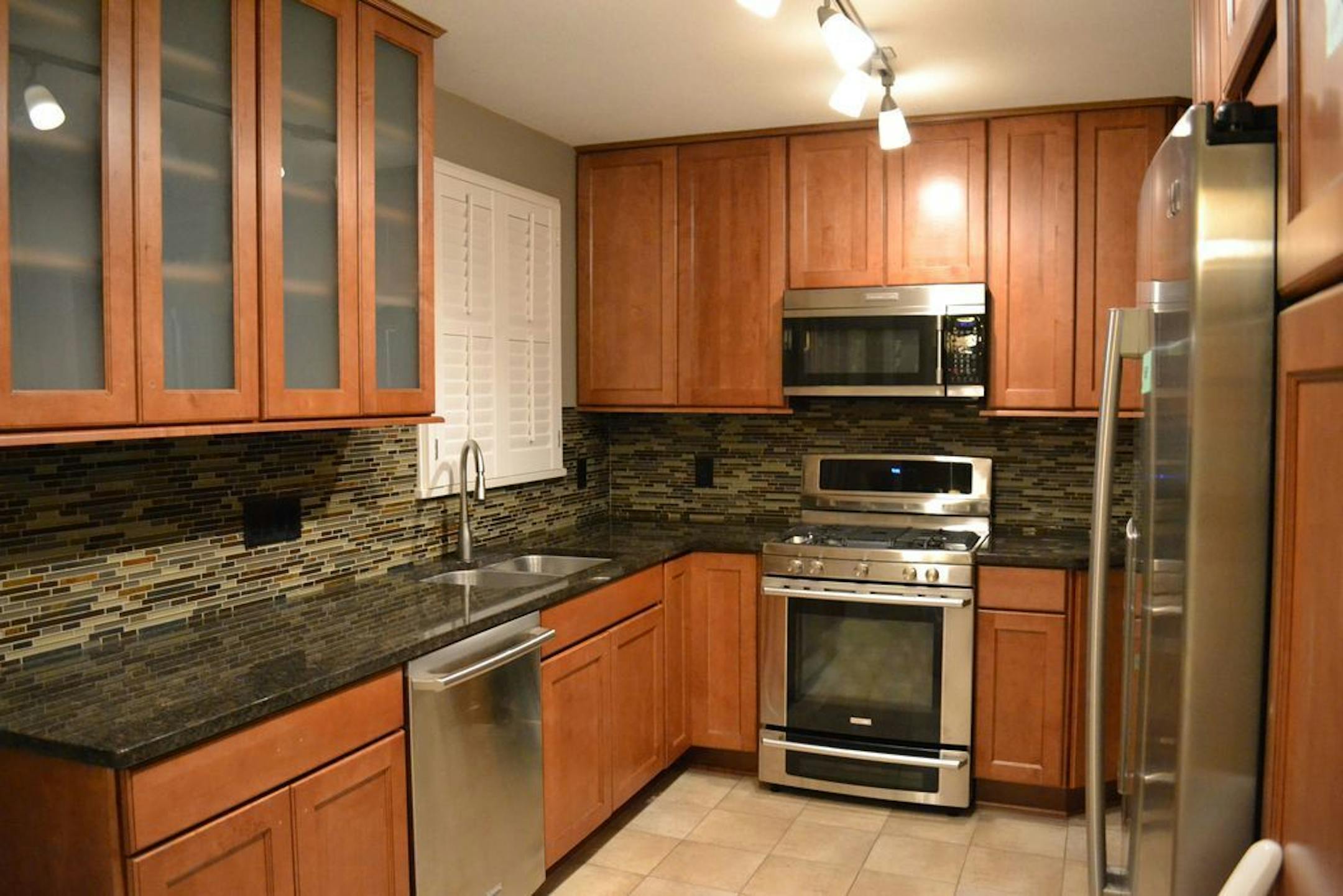 BEFORE - Dark cherrywood cabinets, black and brown granite countertops and glass mosaic tile backsplash.