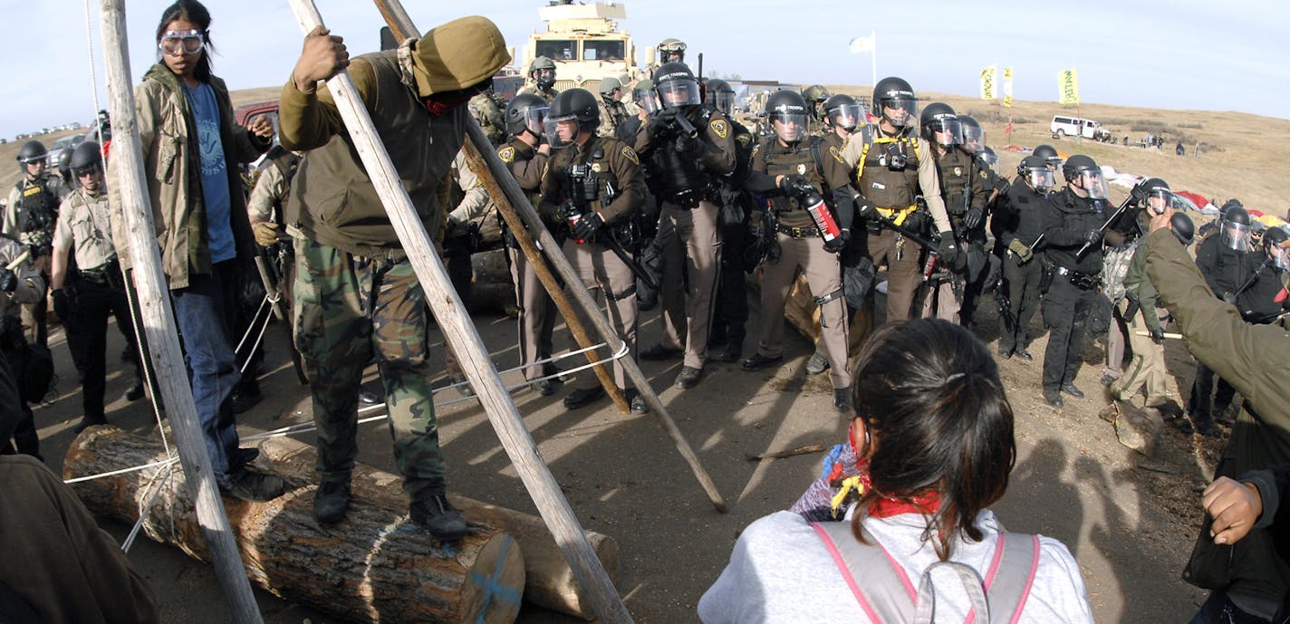 FILE--In this Oct. 27, 2016, file photo, protesters in the left foreground shield their faces as a line of law enforcement officers holding large canisters with pepper spray shout orders to move back during a standoff in Morton County, N.D. On the same day seven defendants celebrated acquittal in Portland, Ore., for their armed takeover of a federal wildlife refuge in Oregon, nearly 150 protesters camped out in North Dakota to protest an oil pipeline were arrested. (Mike McCleary/The Bismarck Tr