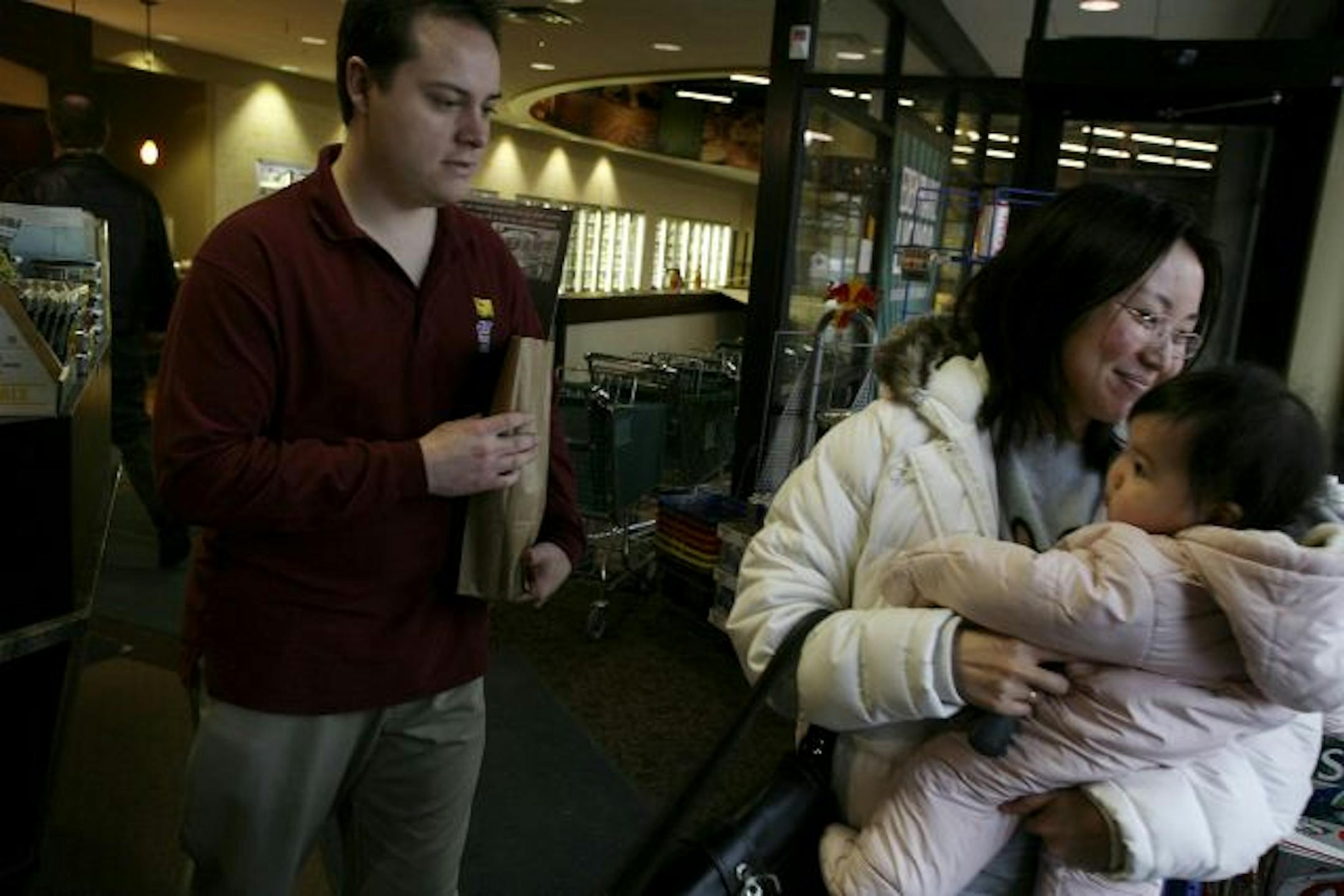 Eden Prairie Liquor employee Scott MacArthur, left, helps customer Megumi Yamamoto, right, who is carrying her 10-month-old daughter Saaya, bring her purchases to her car.