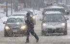 A pedestrian crosses the street in front of vehicles during a snowstorm.
