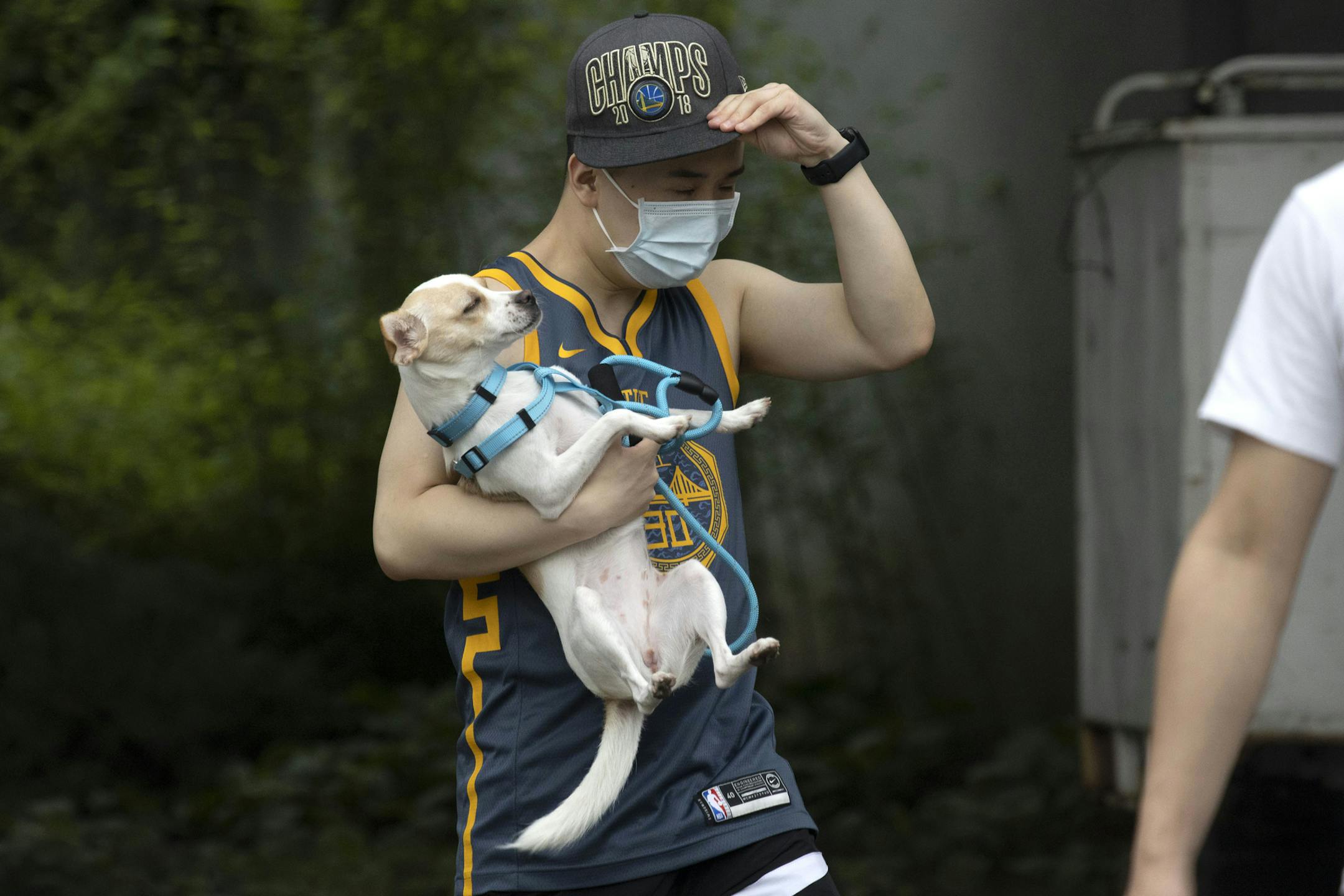 A man wearing a mask carries his dog along a street in Beijing on Thursday, June 25, 2020. In China, where the virus first appeared late last year, an outbreak in Beijing appeared to have been brought under control. China reporting more than a dozen of newly confirmed cases nationwide amid mass testing in the capital. (AP Photo/Ng Han Guan)