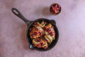 A savory skillet dish featuring chicken and vegetables on a pink background, complemented by the flavors of cherry jam and dijon mustard.