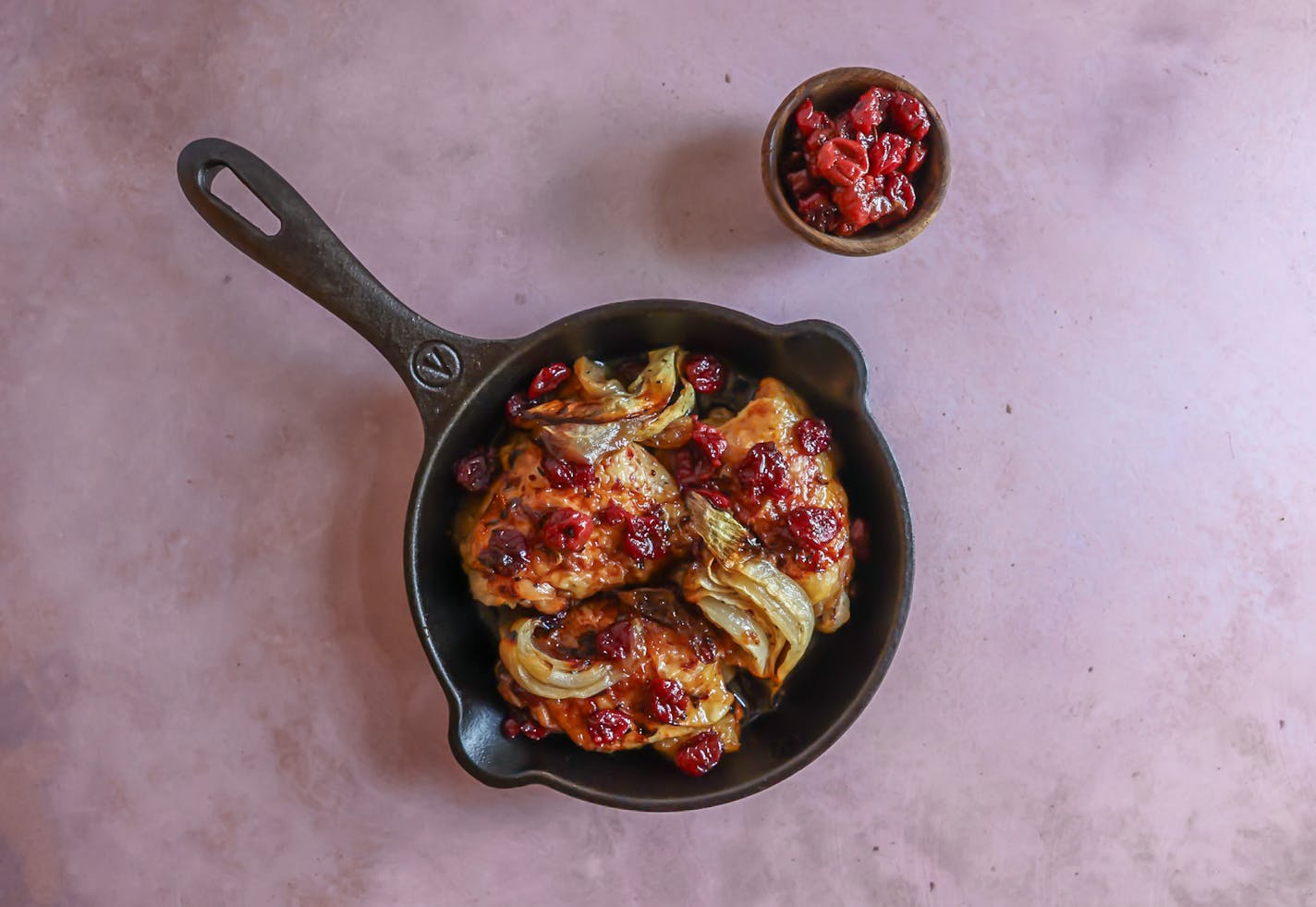 A savory skillet dish featuring chicken and vegetables on a pink background, complemented by the flavors of cherry jam and dijon mustard.