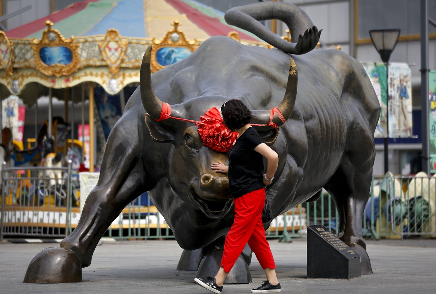 A Chinese woman touches a bull statue on display outside a retail and wholesale clothing mall in Beijing, Monday, June 18, 2018. Asian shares were mostly lower Monday amid worries about trade tensions as the U.S. and China both started putting tariffs in motion. China and Hong Kong markets were closed for a national holiday.(AP Photo/Andy Wong)