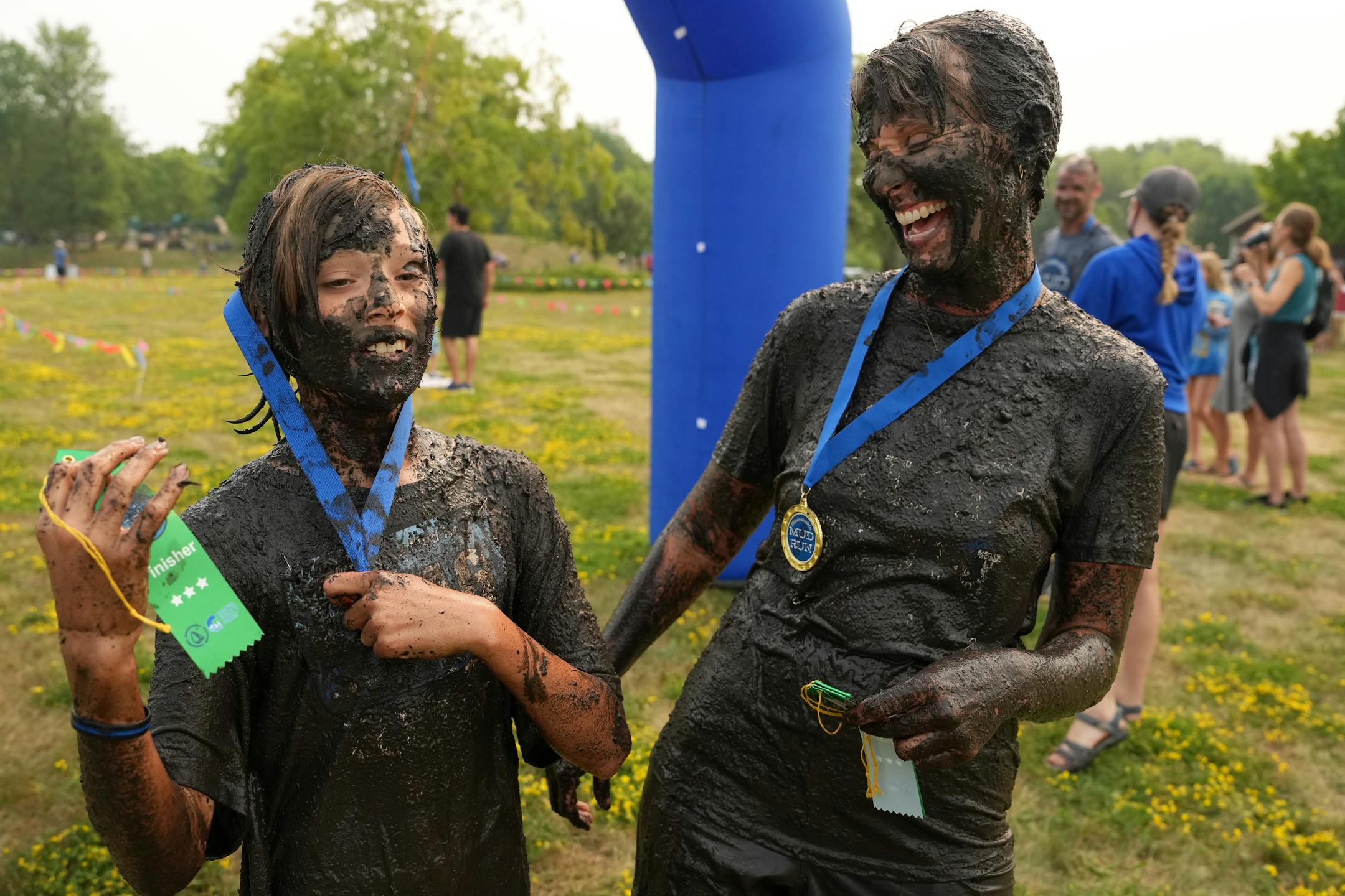 Brianna Kirt of Excelsior laughs as her son Wyatt, 11, tries to put on his medal while covered in mud after running the Minneswashta Mud Run.