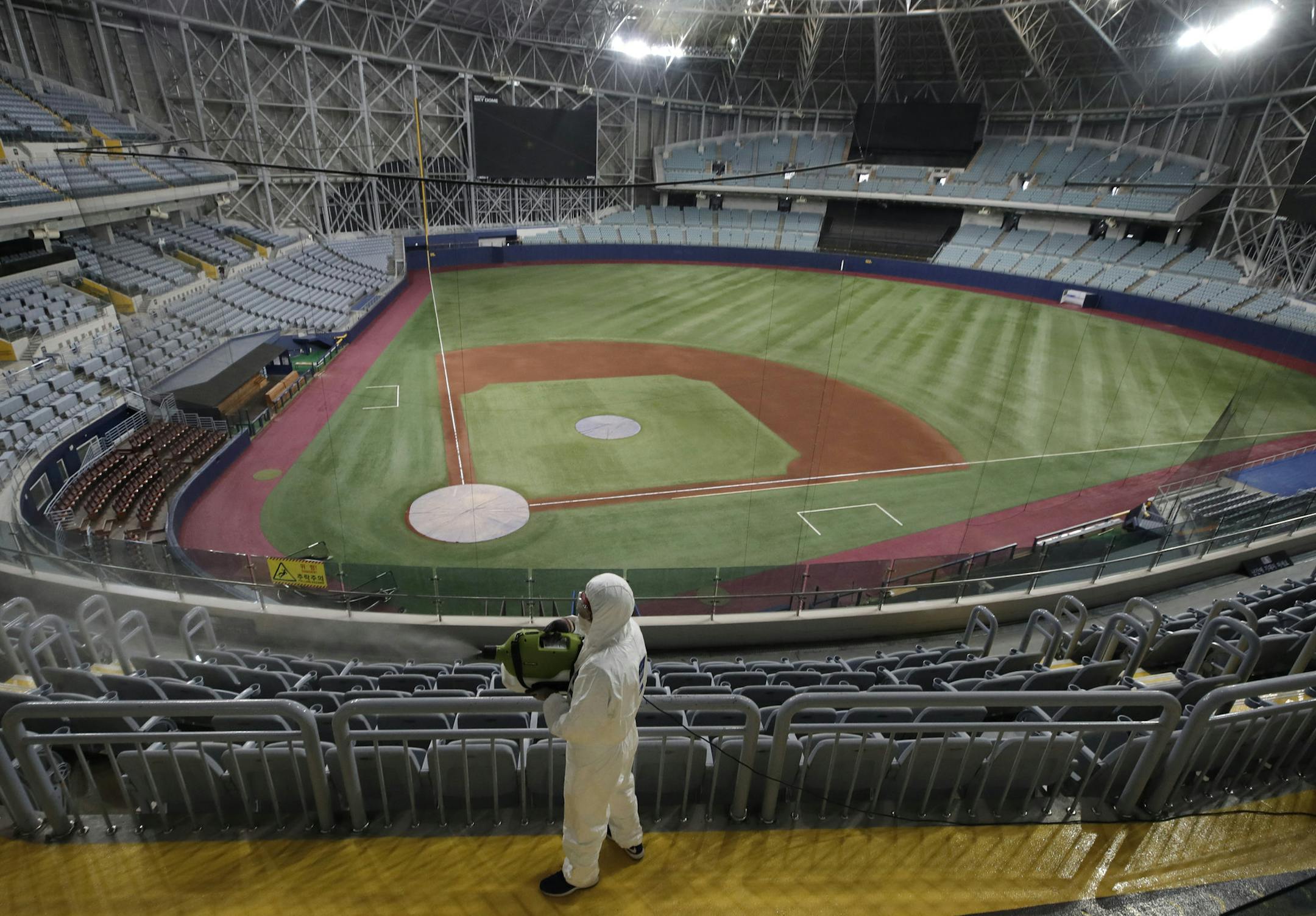 A worker wearing protective gears disinfects as a precaution against the new coronavirus at Gocheok Sky Dome in Seoul, South Korea, Tuesday, March 17, 2020. The Korea Baseball Organization has postponed the start of new season to prevent the spread of the new coronavirus. For most people, the new coronavirus causes only mild or moderate symptoms. For some it can cause more severe illness. (AP Photo/Lee Jin-man) ORG XMIT: LJM101