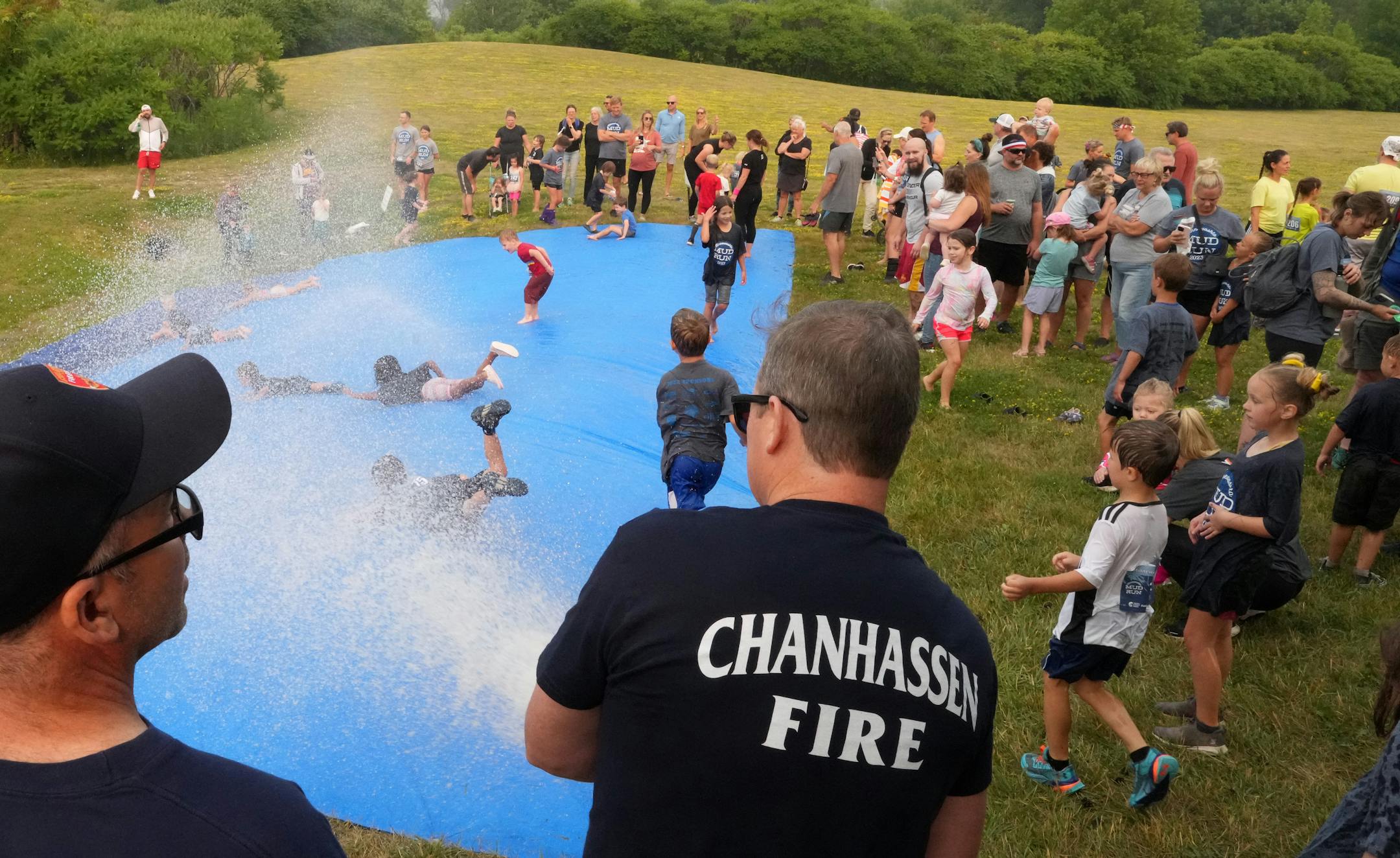 Chanhassen firefighters Bryan O'Keeffe and Dan Ryan use a fire hose to create a giant slip and slide after the Minneswashta Mud Run's Mini Mud Run.