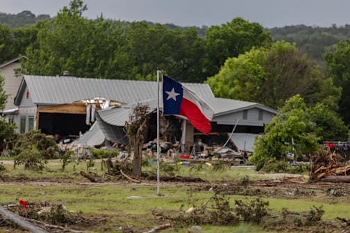 A Texas state flag flies in a yard filled with debris on July 6, 2025, in Hunt, Texas. Heavy rainfall caused flooding along the Guadalupe River in central Texas with multiple fatalities reported.