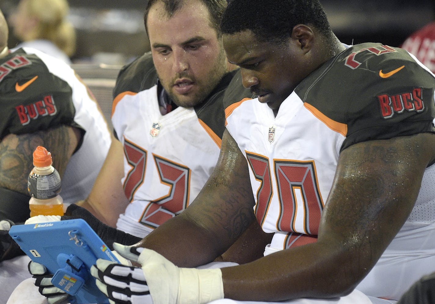 Tampa Bay Buccaneers offensive lineman Ben Gottschalk (72), center, and defensive tackle A.J. Francis (70) view plays on an electronic tablet while sitting on the bench during the second half of an NFL preseason football game against the Jacksonville Jaguars in Jacksonville, Fla., Saturday, Aug. 20, 2016. The Buccaneers won 27-21. (AP Photo/Phelan M. Ebenhack)