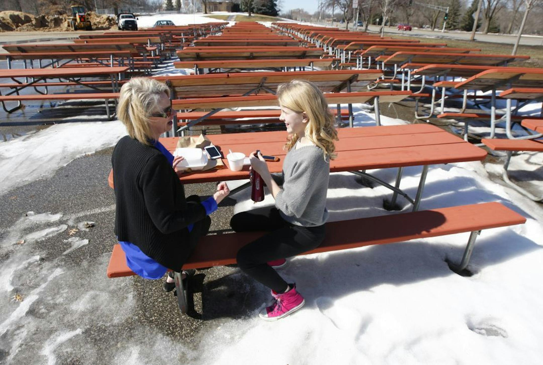 In this March 9, 2015, photo, Carolyn Feigal and her daughter Ella eat lunch in the sunshine and melting snow at Silver Lake in Rochester, Minn., where picnic tables are still stacked for the winter in the parking lot.
