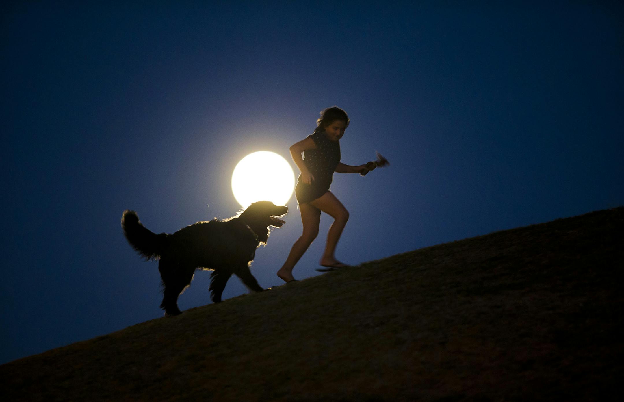 A girl plays with a dog as a perigee moon, also known as a supermoon, rises in Madrid, Sunday, Aug. 10, 2014. The phenomenon, which scientists call a perigee moon, occurs when the moon is near the horizon and appears larger and brighter than other full moons. (AP Photo/Andres Kudacki)