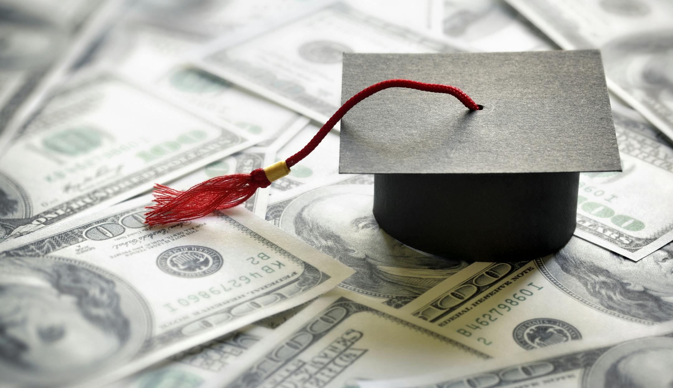 Graduation mortar board cap on one hundred dollar bills concept for the cost of a college and university education. istock photo