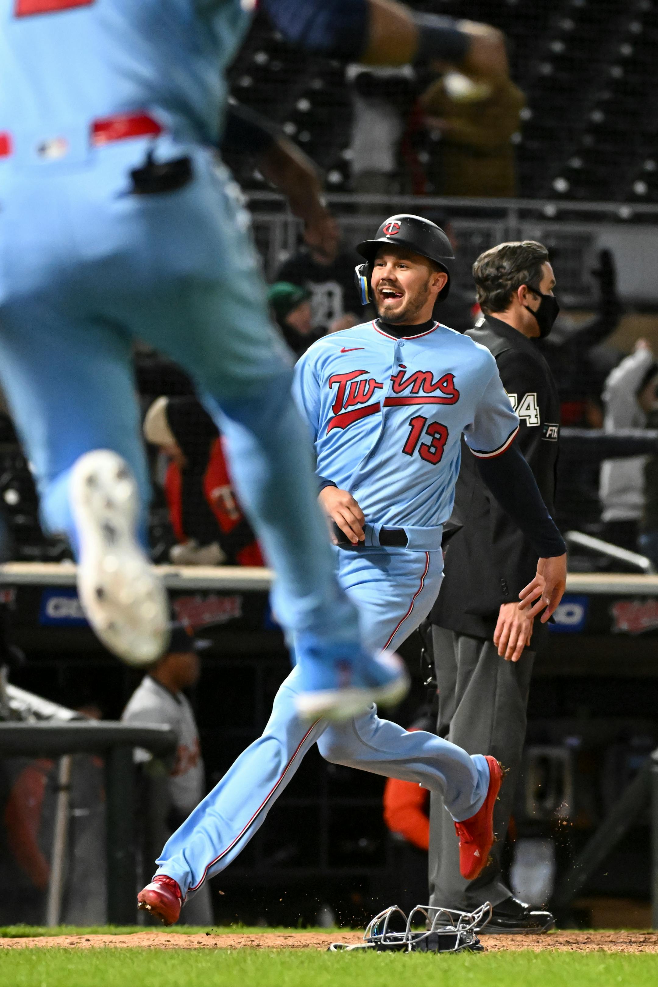 Minnesota Twins left fielder Trevor Larnach (13) scores a run and celebrates after a throwing error by Detroit Tigers catcher Eric Haase (13) leading to a 5-4 walk-off win, with third baseman Gio Urshela (15) scoring behind Larnach.