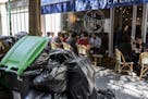 People have lunch past overflowing garbage cans and rubbish bags in Paris, France, Thursday, June 9, 2016. After a rough couple of months which have i