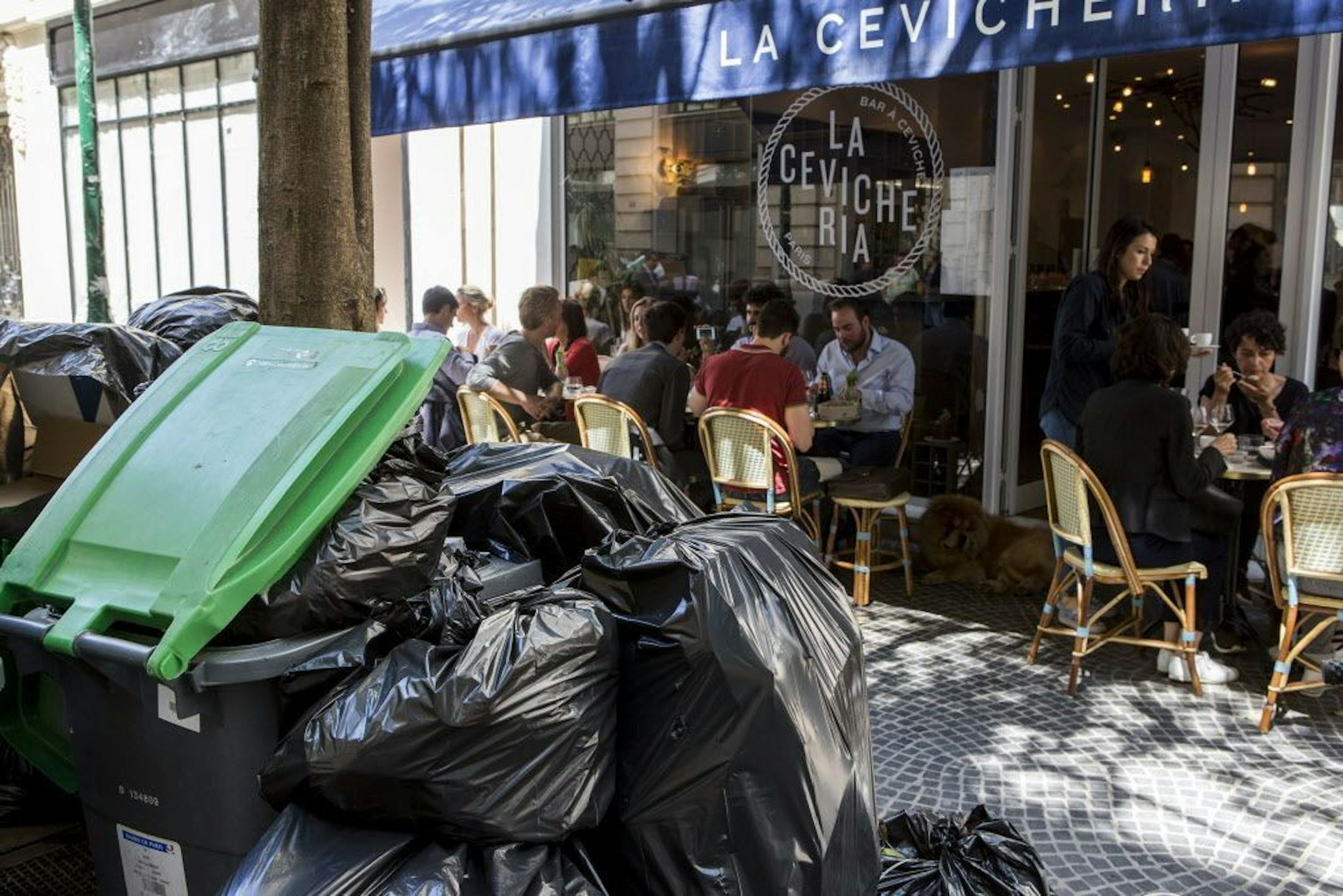 People have lunch past overflowing garbage cans and rubbish bags in Paris, France, Thursday, June 9, 2016. After a rough couple of months which have included protests, fuel shortages, rail strikes and once-in-a-generation floods, France's capital is facing a new challenge : Piles of uncollected trash.