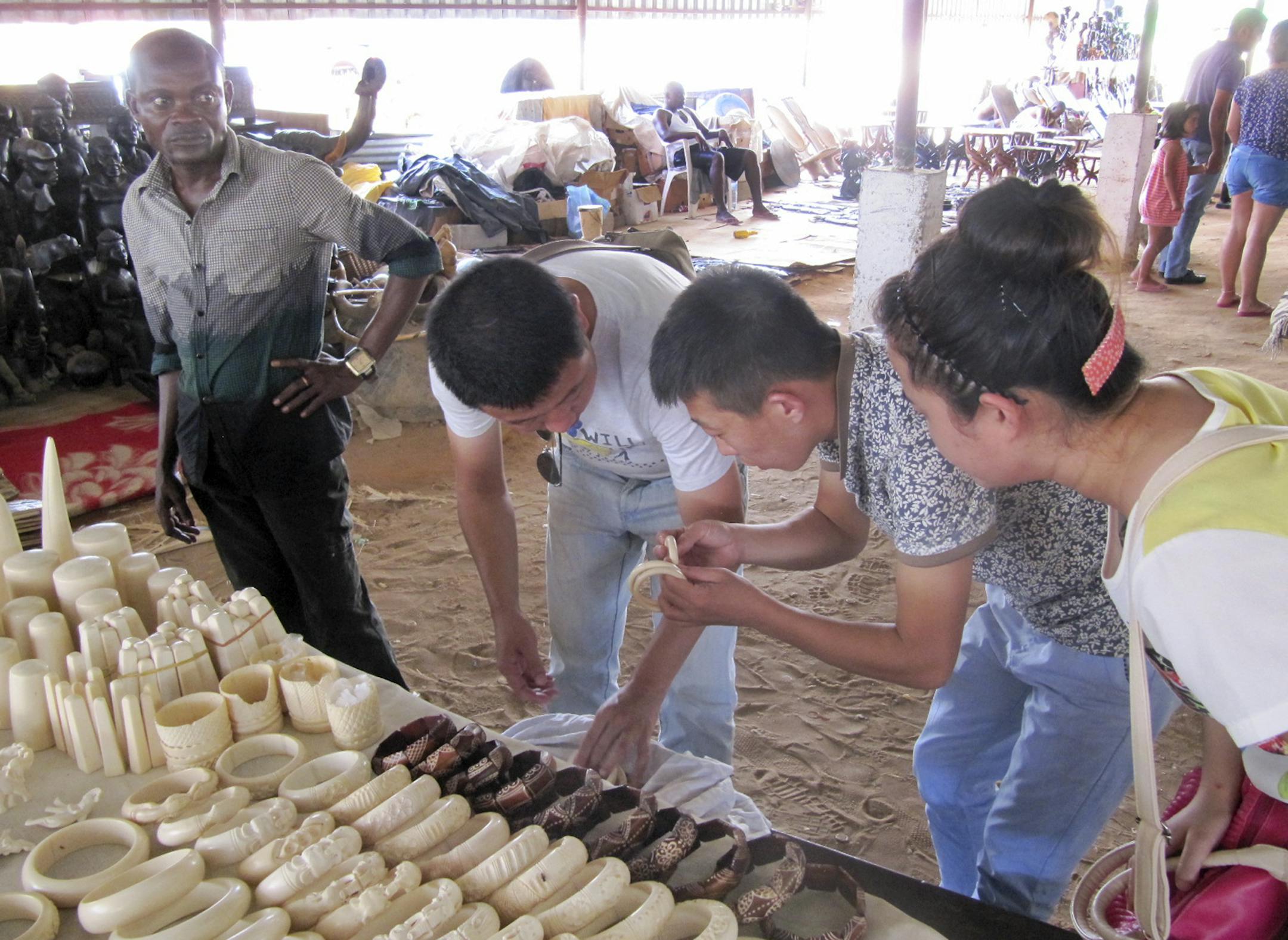 In this photo taken Thursday, Feb. 27, 2014 and provided by Esmond Martin, A market seller, left, watches as Chinese visitors observe souvenirs made of ivory for sale at the Benfica market on the outskirts of Luanda, Angola. The market on the outskirts of Angolaís capital sells more than 10,000 pieces of ivory, making it the largest market in southern Africa to openly sell illegal elephant tusks, according to two researchers who traveled to Luanda and surveyed the items of ivory for sale, s