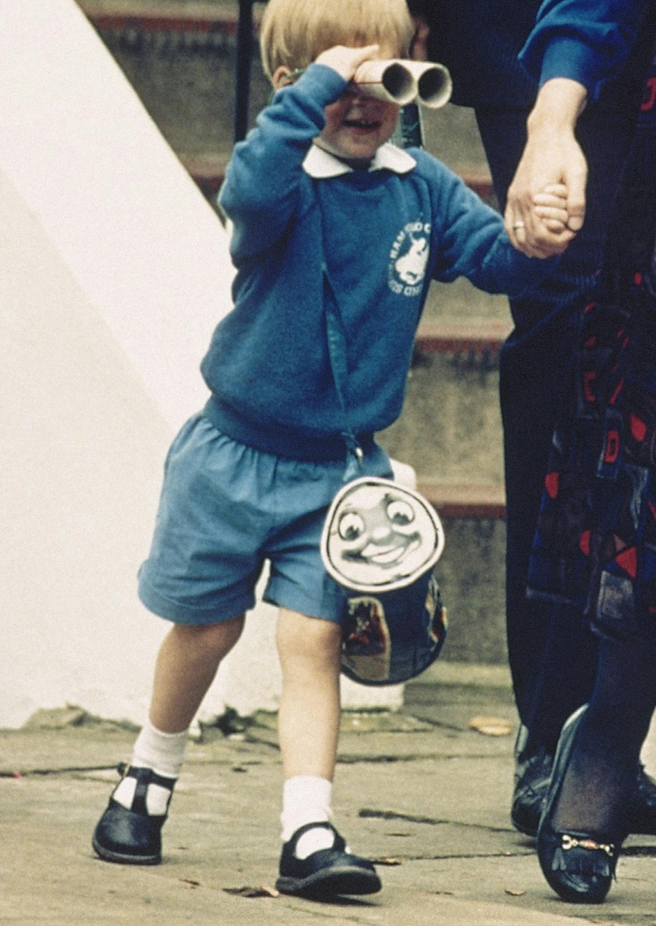 FILE - In this Sept. 16, 1987 file photo, Britain's Prince Harry looks through mock binoculars whilst holding the hand of Kindergarten manager Jane Mynors and carrying a 'Thomas The Tank Engine' bag on his way out from his first day at a kindergarten in Notting Hill, West London. Britain's Prince Harry has recorded a special message to celebrate the 75th anniversary of Thomas The Tank Engine, introducing a new program called 'Thomas And Friends: The Royal Engine' that includes the Queen Elizabet