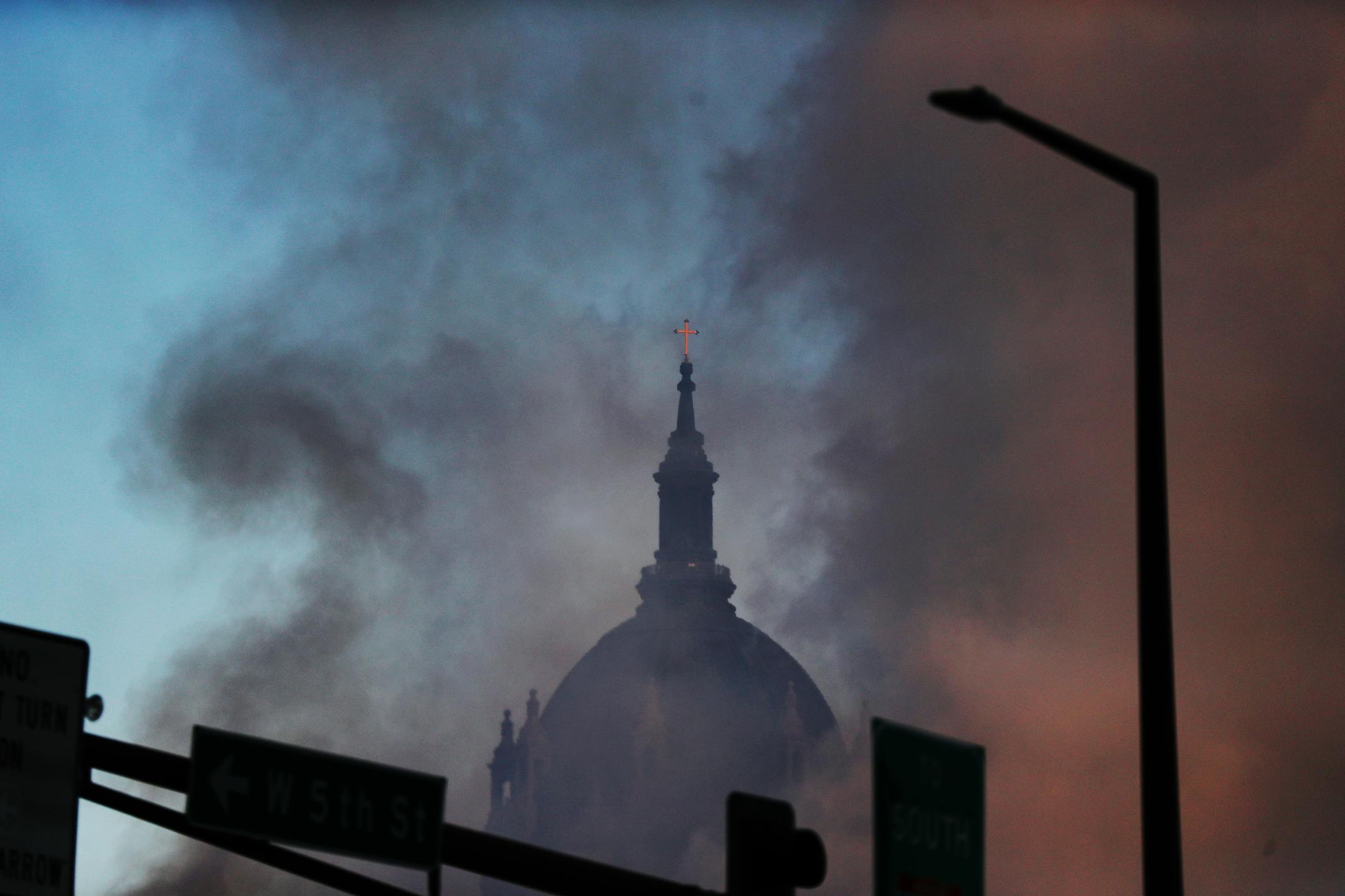 Fire ripped through a $69 million project hotel/apartment project early Tuesday morning, causing massive damage near the Xcel Energy Center in St. Paul. Here, smoke from the fire obscures the nearby Cathedral of Saint Paul.