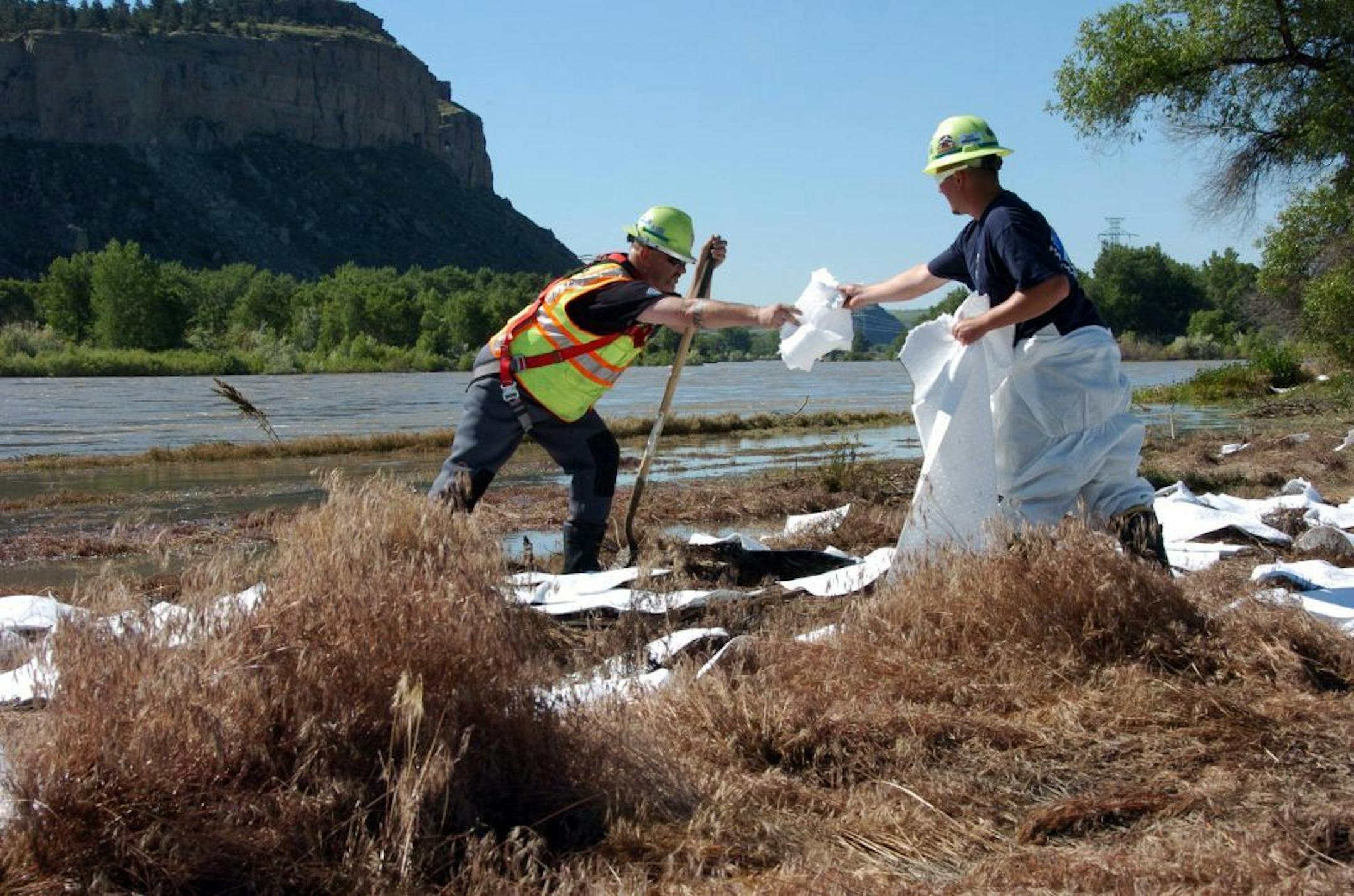 ExxonMobil contractors spread absorbent pads to soak up oil along the banks of the Yellowstone River in Billings, Mont., Sunday, July 3, 2011.
