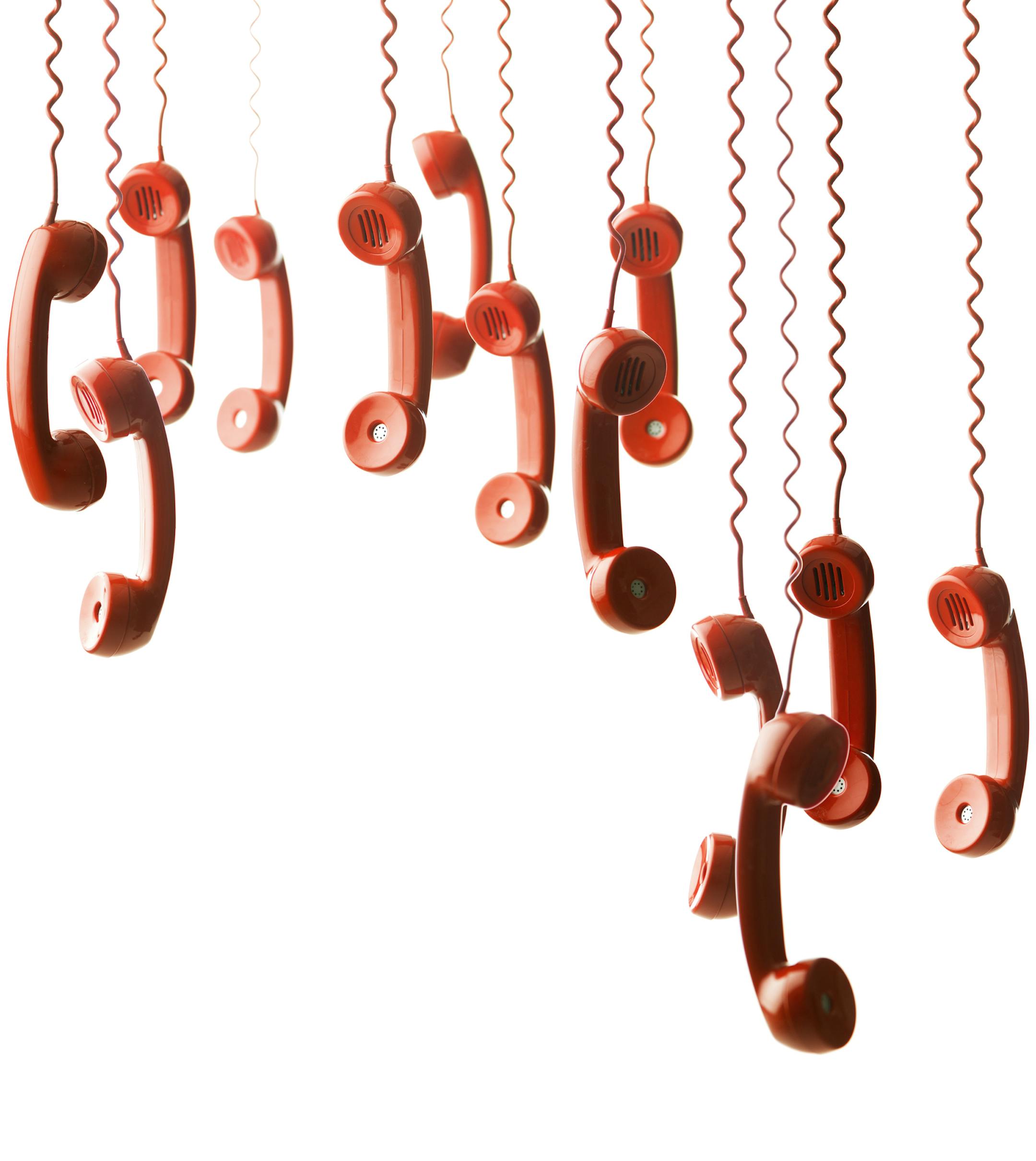 group of red handsets from vintage phones hanging against white background. iStock