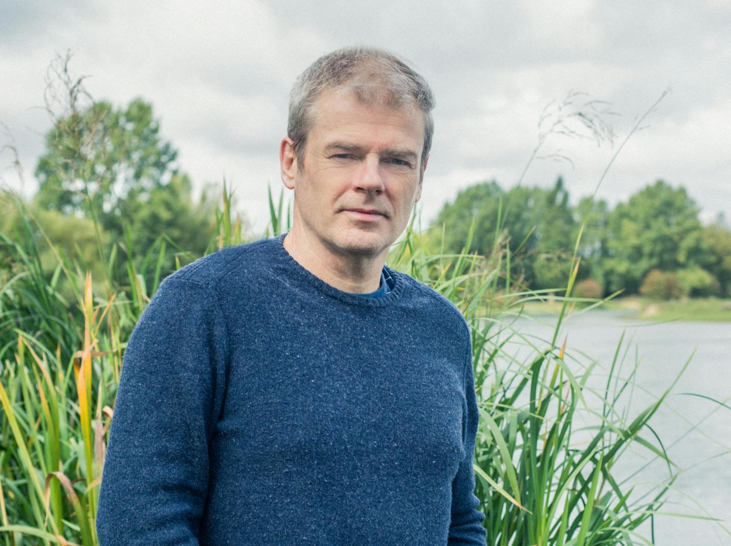 photo of author Mark Haddon, with a body of water and greenery in the background