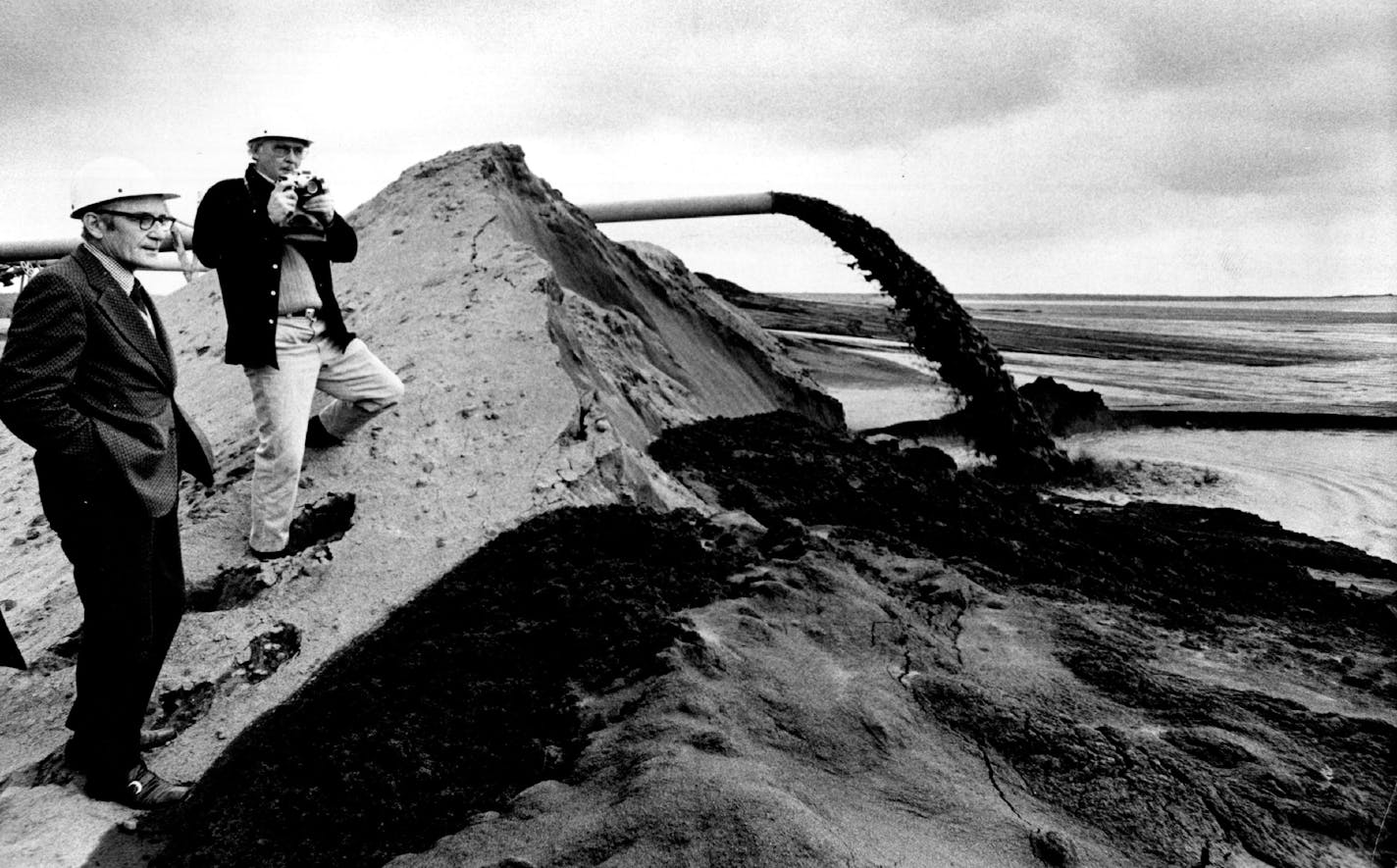 in 1973, Judge Miles Lord (left) and federal attorney John Hills viewed on-land disposal of taconite tailings at Hoyt Lakes, a method seen as impractical by Reserve Mining for its Silver Bay plant, where a similar stream gushed directly into Lake Superior. From the first enforcement action in 1969 to stop the Silver Bay disposal, it took 11 years to turn off the tailings chutes.