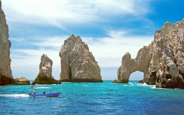 Inside the bay at Cabo San Lucas, Mexico, a tourboat is dwarfed by rock formations including El Arco.