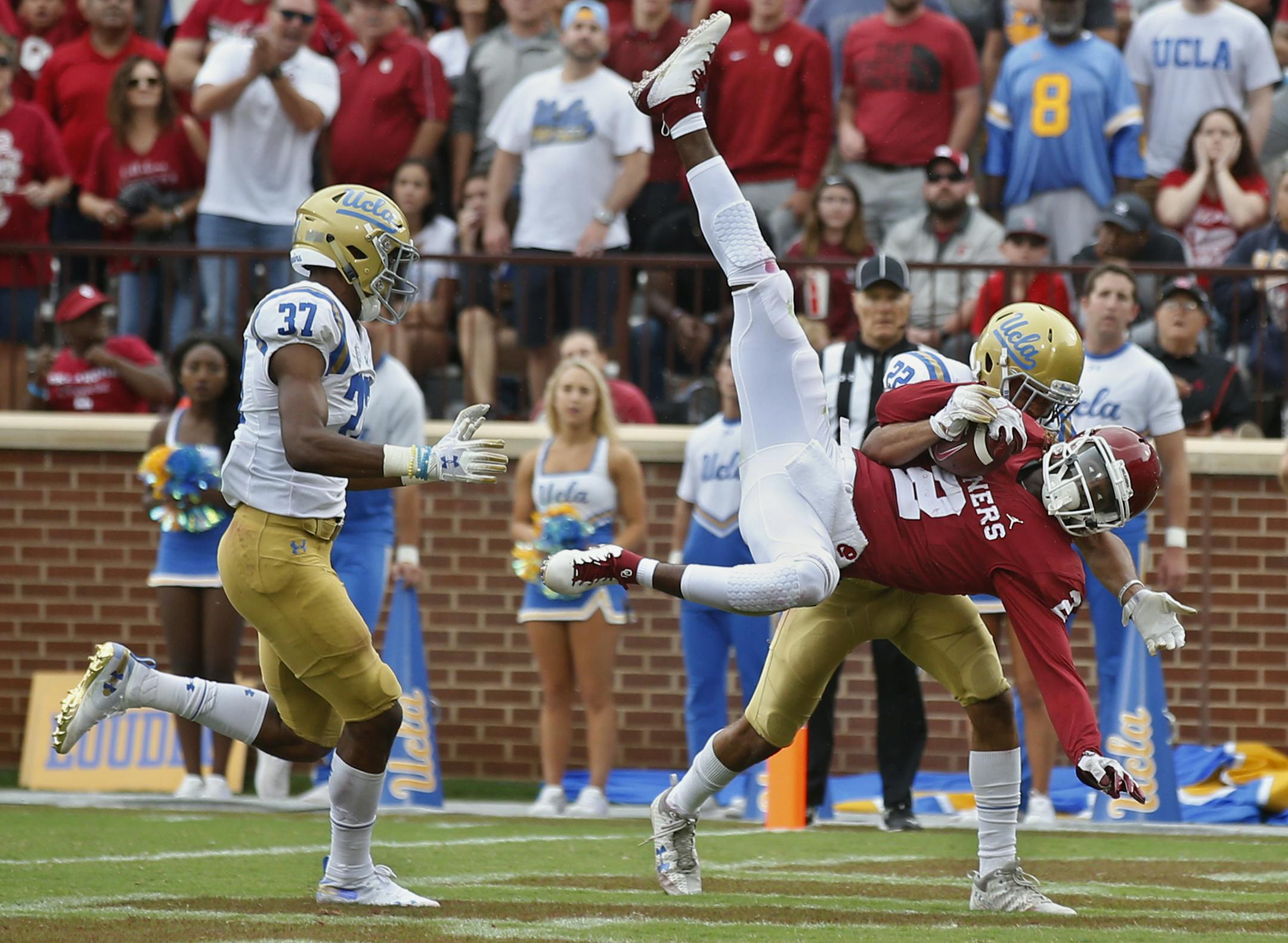 Oklahoma wide receiver CeeDee Lamb (2) comes down with a touchdown pass in front of UCLA defensive back Nate Meadors (22), rear, and defensive back Quentin Lake (37) in the second half of an NCAA college football game in Norman, Okla., Saturday, Sept. 8, 2018. Oklahoma won 49-21. (AP Photo/Sue Ogrocki)