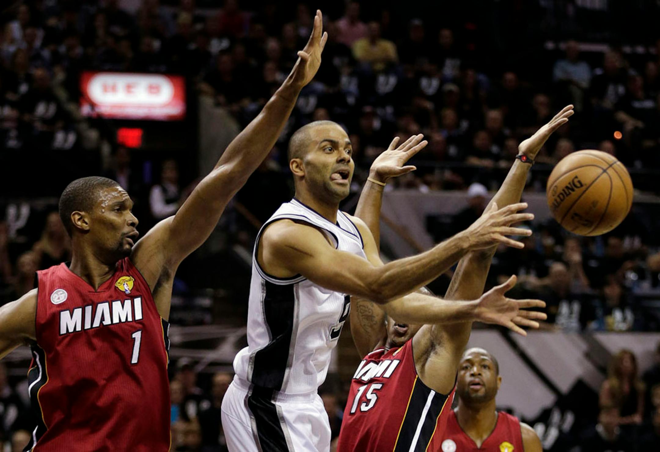 San Antonio Spurs' Tony Parker (9) passes the ball against Miami Heat's Chris Bosh (1) and Mario Chalmers (15) during the first half.