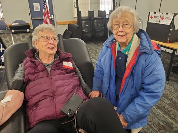 Barbara Swartwoudt sits in a chair donating blood while Cindy Anderson accompanies her.