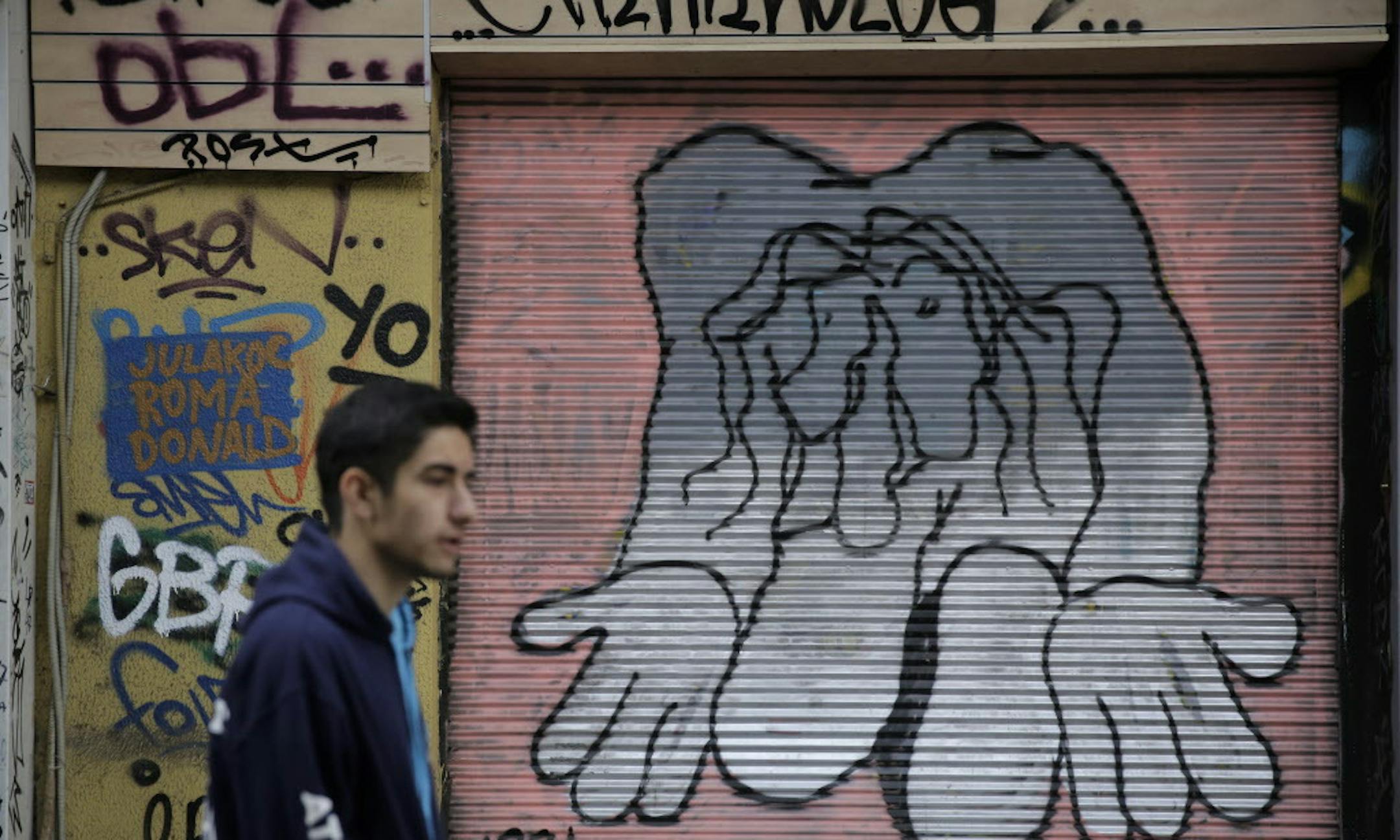 A man walks past a shop with its shutter painted with a mural, in central Athens on Monday, March 9, 2015. Eurozone finance ministers will discuss about Greece at a Eurogroup meeting on Monday, as Athens had submitted seven reform proposals. (AP Photo/Petros Giannakouris)