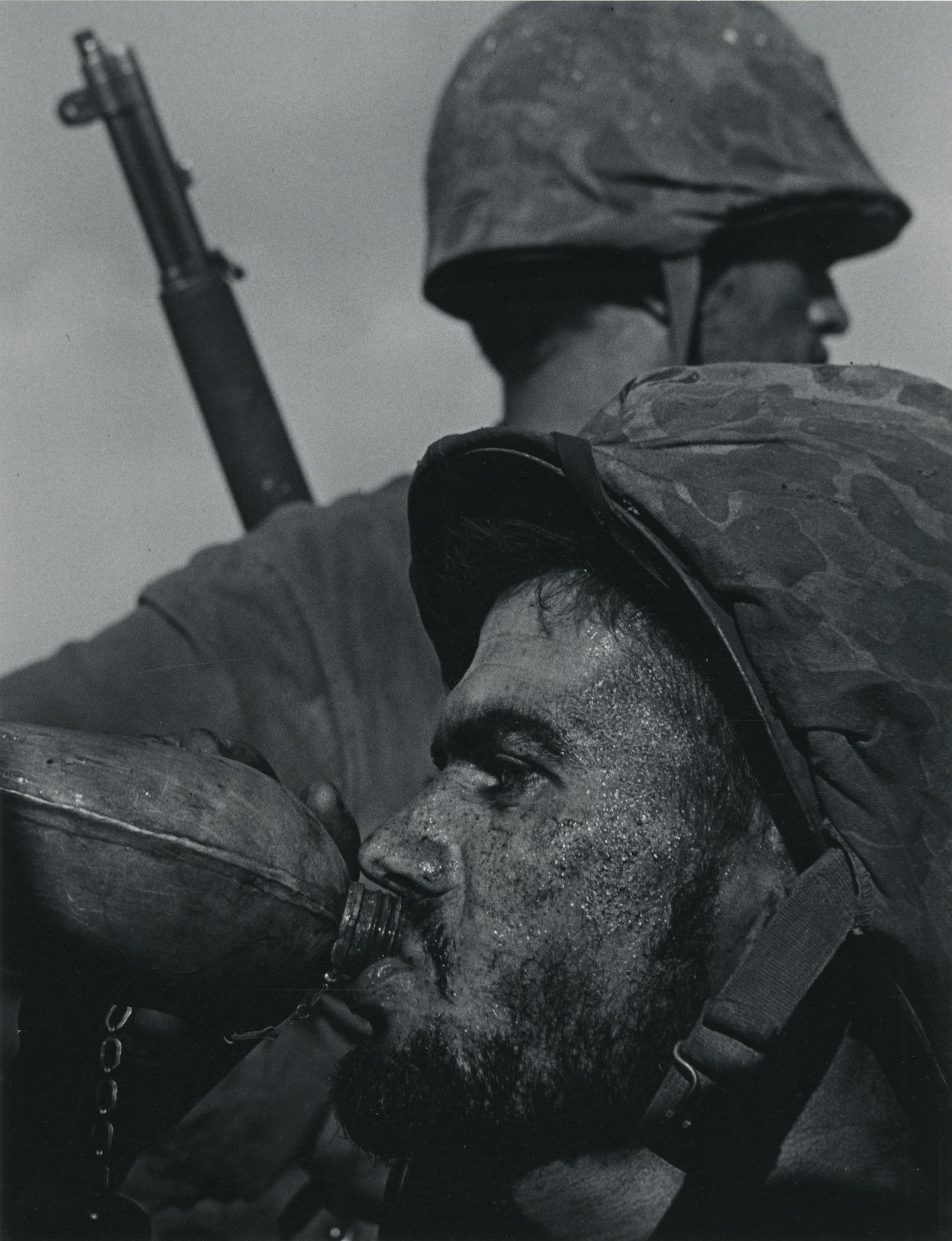 Photo by W. Eugene Smith provided by Weinstein Gallery. Sweat-stained GI swigging from a canteen as a buddy scans the horizon.