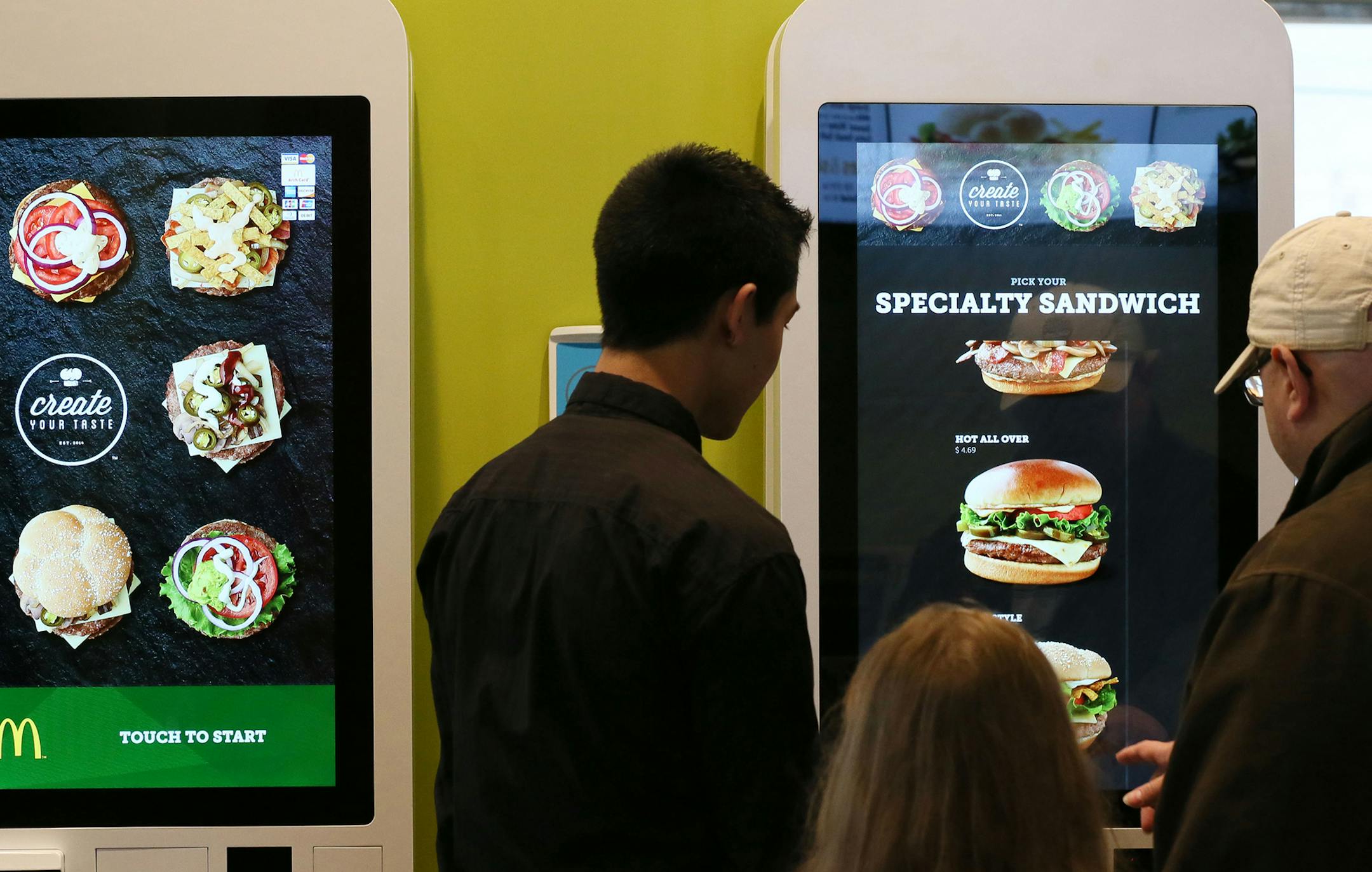 McDonald's worker Sam Shin, left, helps London Cage, right, and his 7-year-old daughter, Charlotte Cage, use the Create Your Taste self-ordering kiosk at the McDonald's in Downers Grove, Ill., on Tuesday, Dec. 16, 2014. This McDonald's is a test site for the new self-ordering kiosk. (Stacey Wescott/Chicago Tribune/TNS) ORG XMIT: 1161484 ORG XMIT: MIN1412172304000431