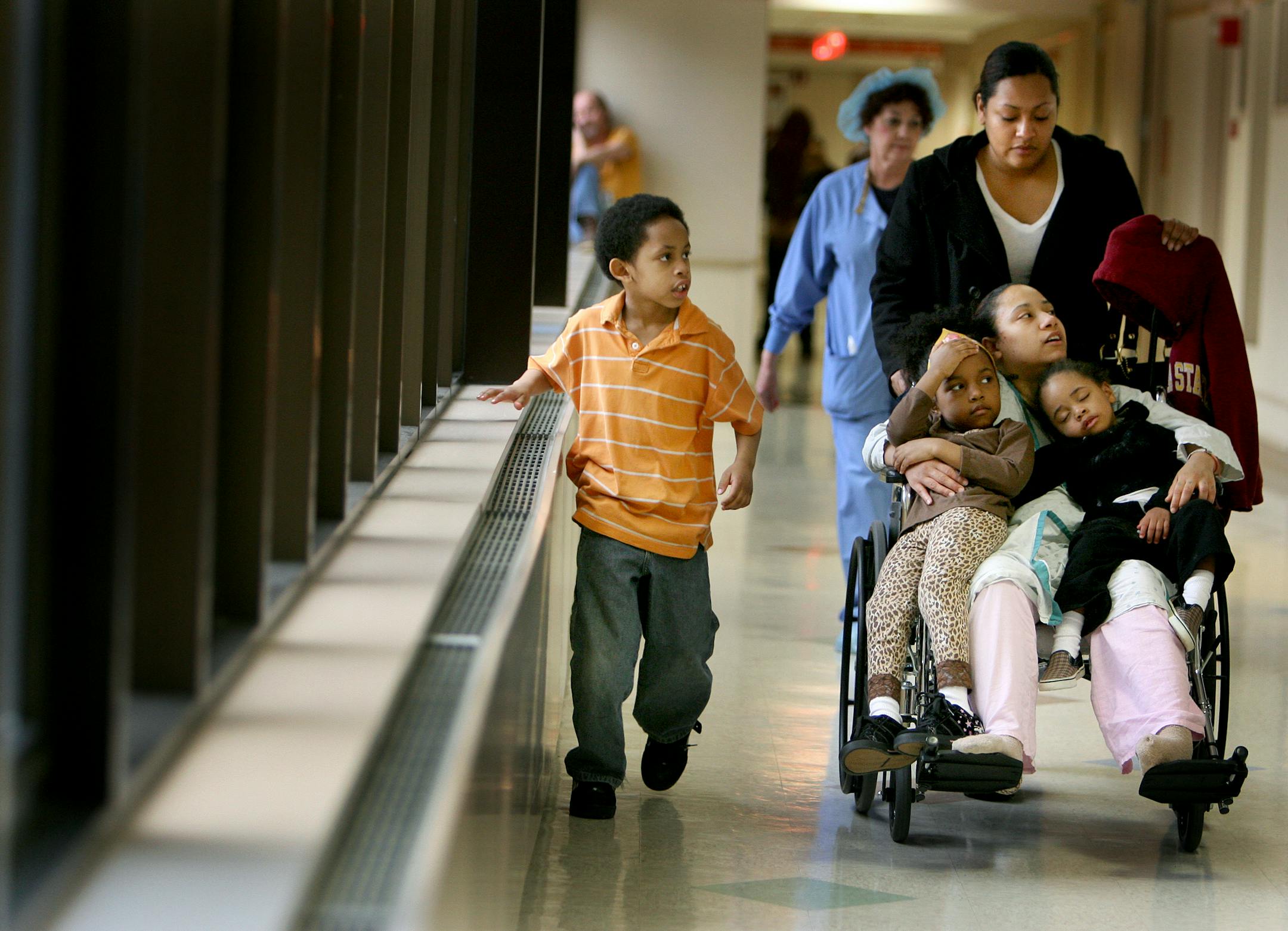 Devon Straub, holding her two of her three children, Janiyah Taylor-Straub, 6, left, and Jerry Straub, received help with a push from her sister Monique Taylor and her son Kevin Robinson, 7 down a corridor at Hennepin County Medical Center.